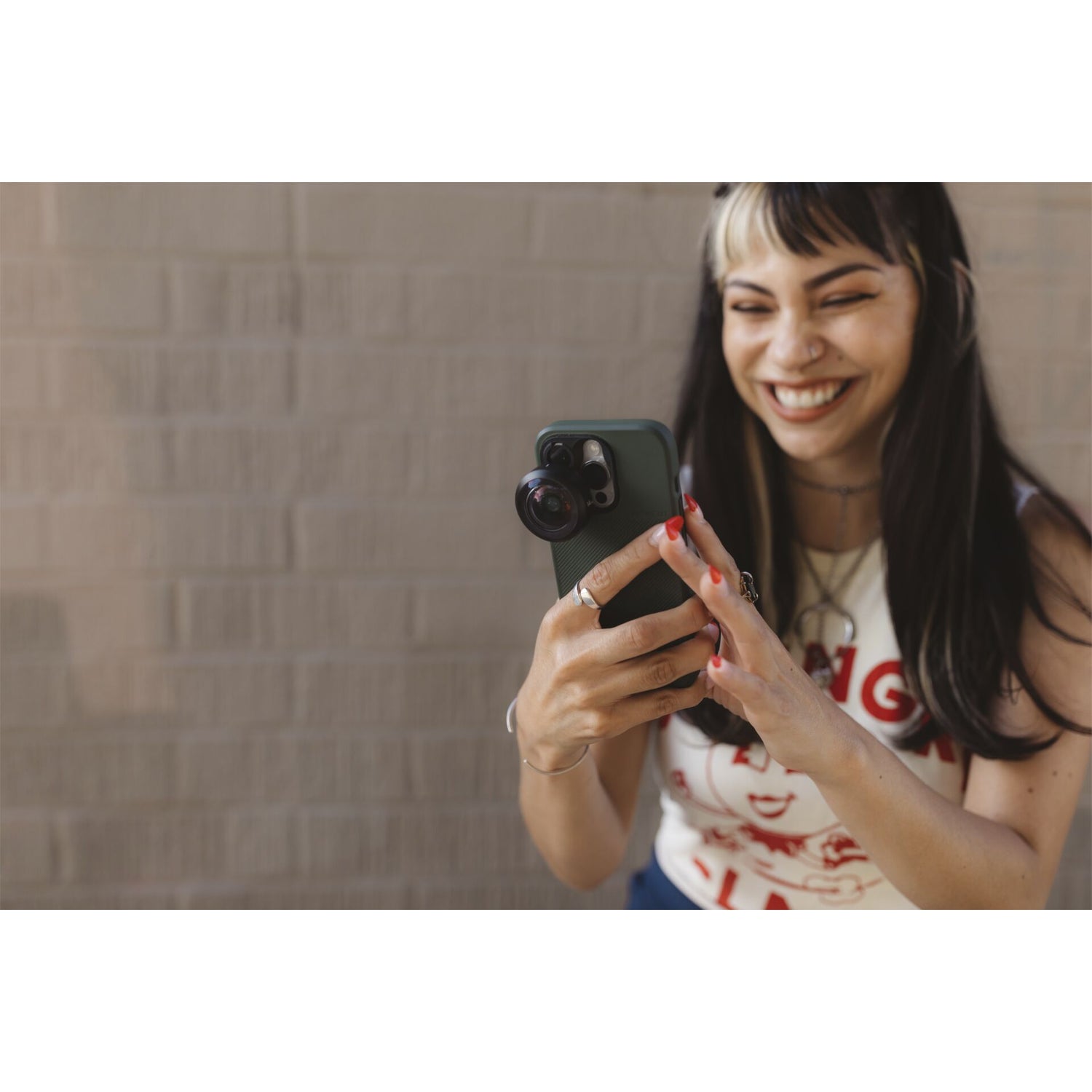 Lächelnde Frau, die ein Foto mit ihrem Smartphone macht. Sie verwendet das MOMENT Moment 14mm Fisheye-Objektiv - T-Serie als iPhone Kamera Zubehör, um eine beeindruckende Weitwinkelaufnahme zu machen.