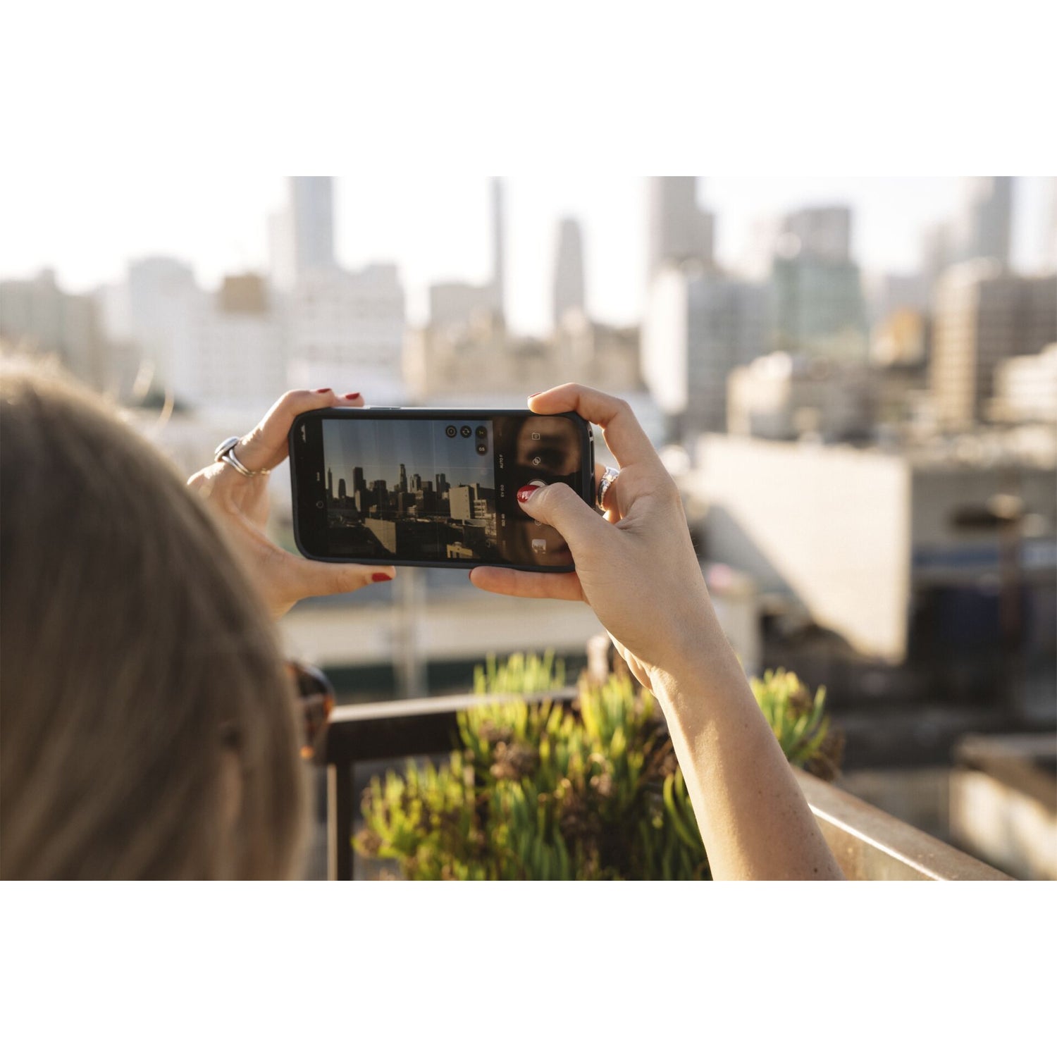 Eine Person macht tagsüber von einem Dach aus ein Foto der Stadtsilhouette mit dem MOMENT 14-mm-Fisheye-Objektiv - T-Serie auf ihrem Smartphone.