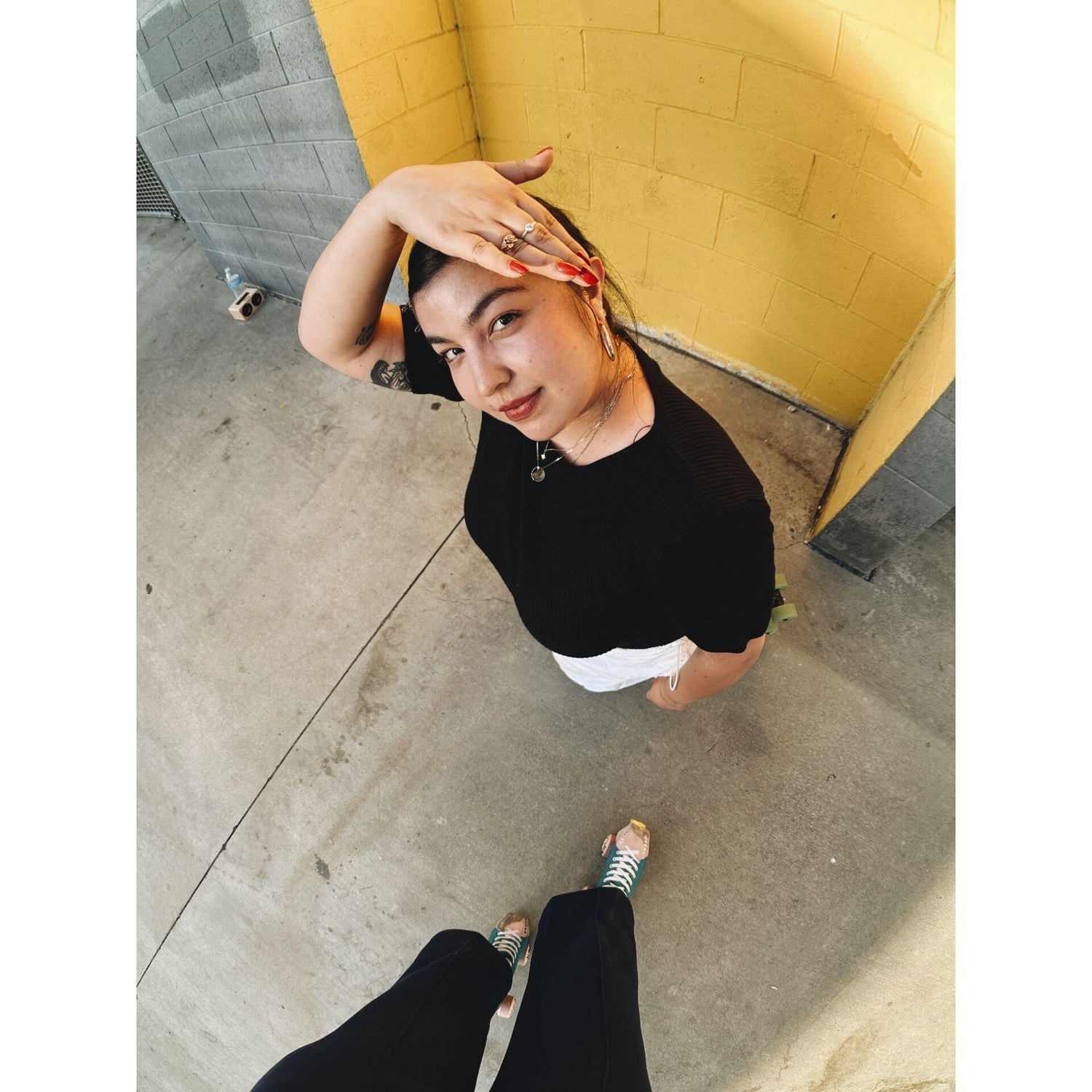 Eine Person in einem schwarzen Hemd steht auf dem Bürgersteig vor einer gelben Wand und schützt ihr Gesicht vor der Sonne - aufgenommen mit dem MOMENT 14mm Fisheye-Objektiv - T-Serie für einen atemberaubenden Weitwinkeleffekt.