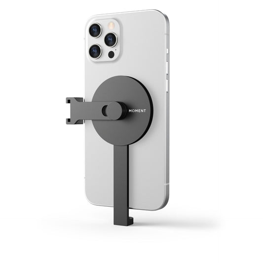 Ein silbernes Smartphone mit der MOMENT Pro Stativhalterung für MagSafe in Schwarz auf der Rückseite, perfektes iPhone Fotografie Zubehör, isoliert auf einem weißen Hintergrund.