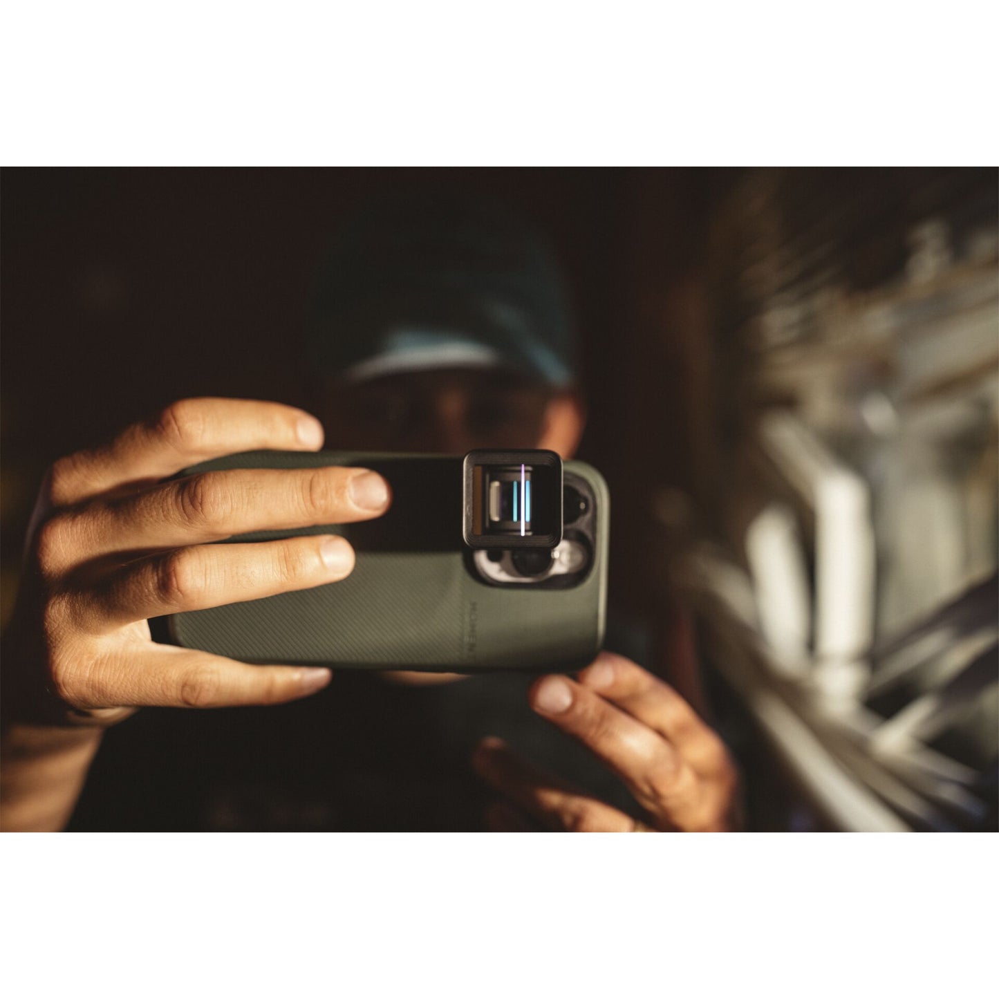 Eine Person, die ein MOMENT Moment 1,33x Anamorphotisches Objektiv der T-Serie auf einem Smartphone hält, macht gerade ein Foto in der Nähe eines Fensters.