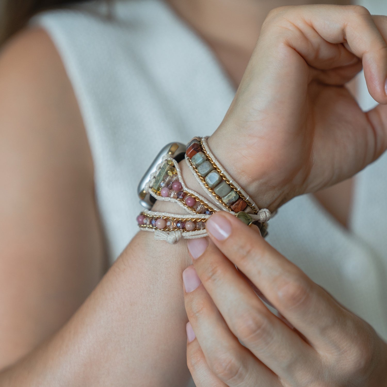 Eine Person befestigt das arktisband Apple Watch Armband "Dream Catcher" von arktisband an ihrem Handgelenk, gestylt mit einem ärmellosen weißen Top.