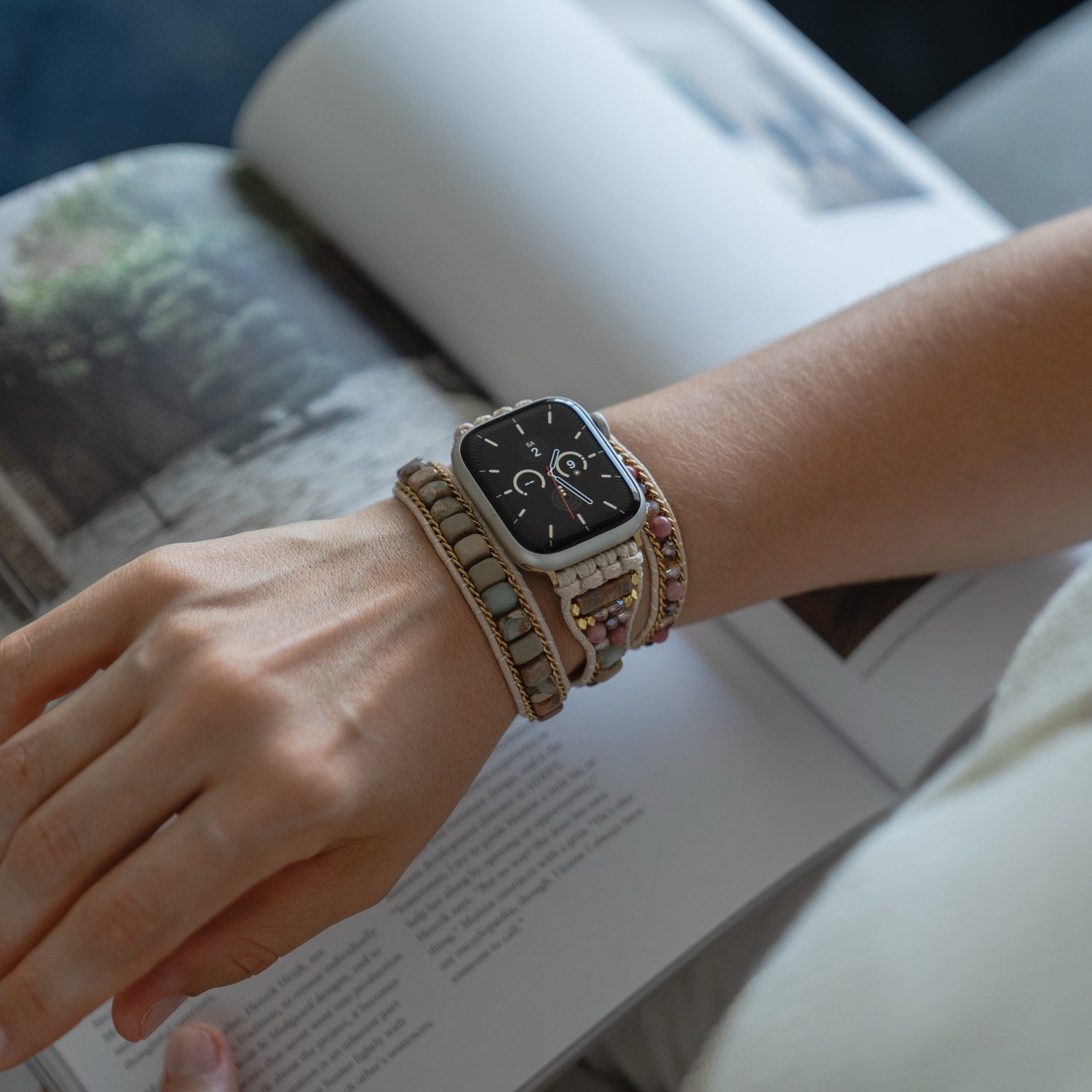 Eine Person, die ein Boho-Armband und das arktisband Apple Watch Armband "Dream Catcher" von arktisband trägt, liest eine Zeitschrift mit einem bezaubernden Naturfoto.