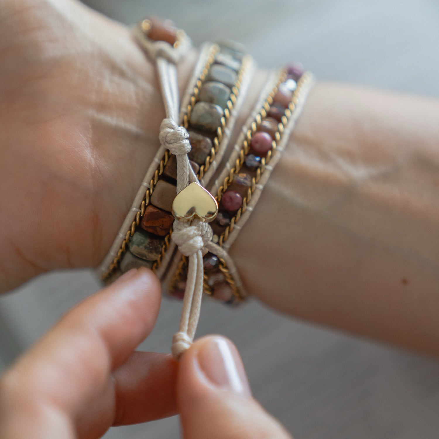 Eine Hand bindet ein stilvolles Boho-Arktisband Apple Watch Armband "Dream Catcher" mit einem goldenen Herzanhänger um das Handgelenk und kombiniert es mühelos zu einem schicken Lagenlook.