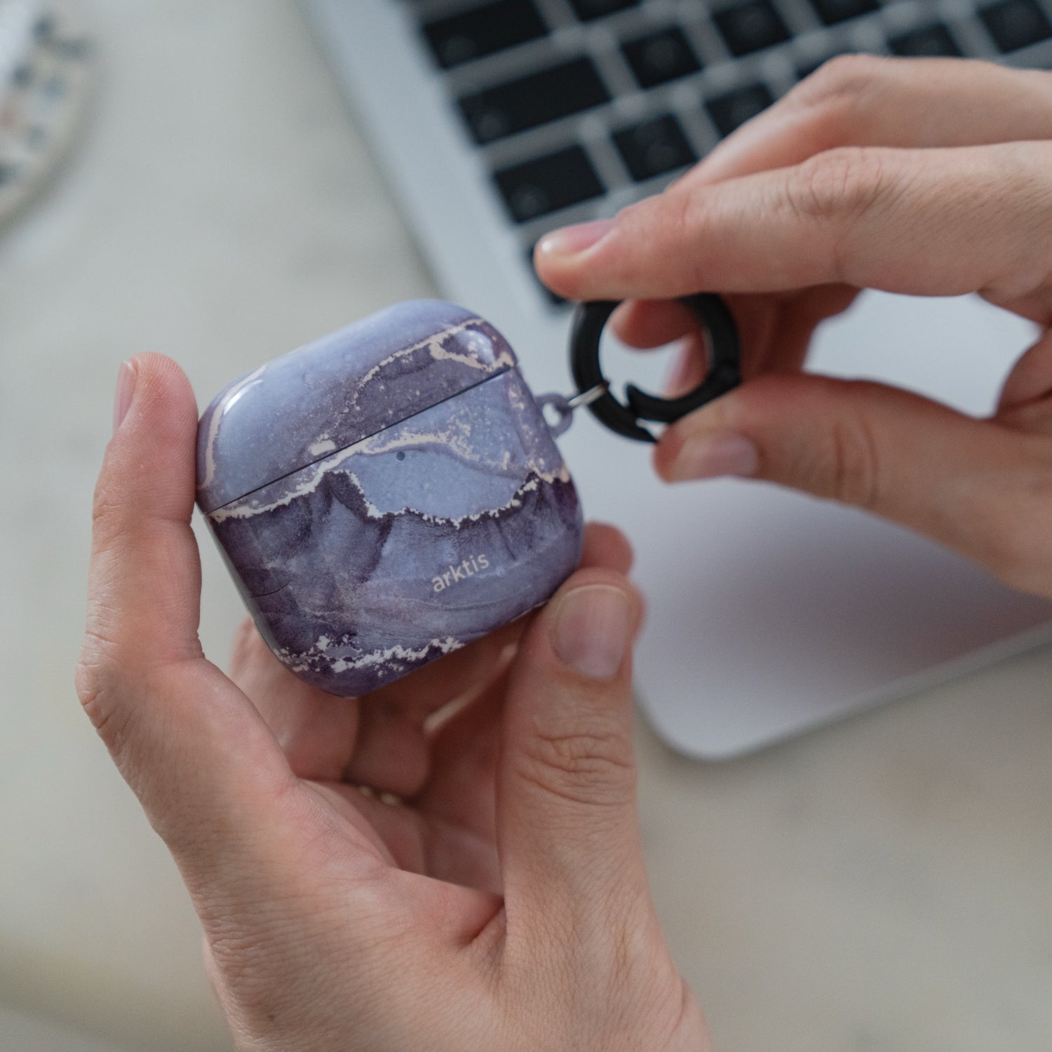Hände, die eine Arktis AirPods 5-Hülle – Dusty Marble – mit violettem Marmormuster und einem angebrachten Ring halten.