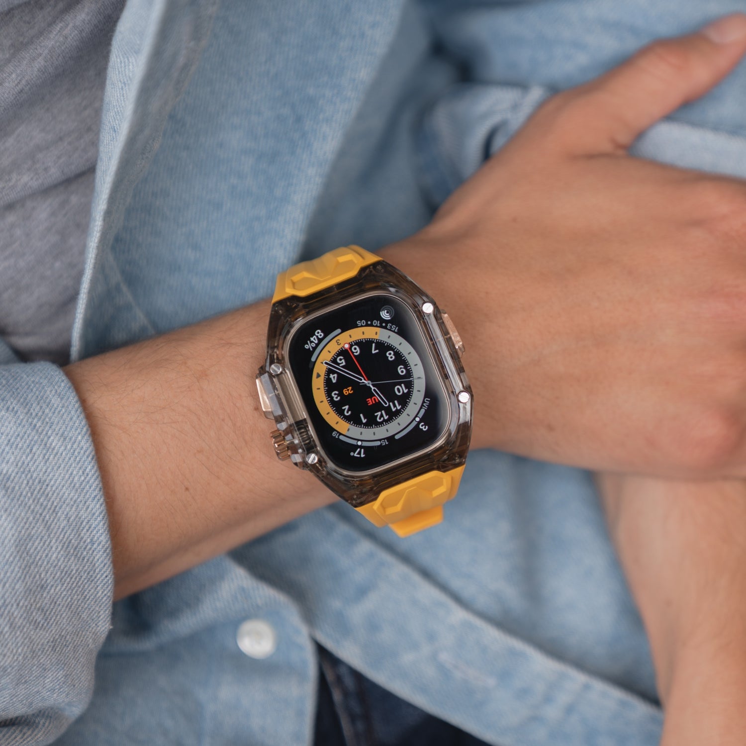Eine Person trägt das arktisband Apple Watch Armband "Armor Fusion" von arktisband mit buntem Zifferblatt und transparentem Hardcase am Handgelenk, bekleidet mit einer Jeansjacke.