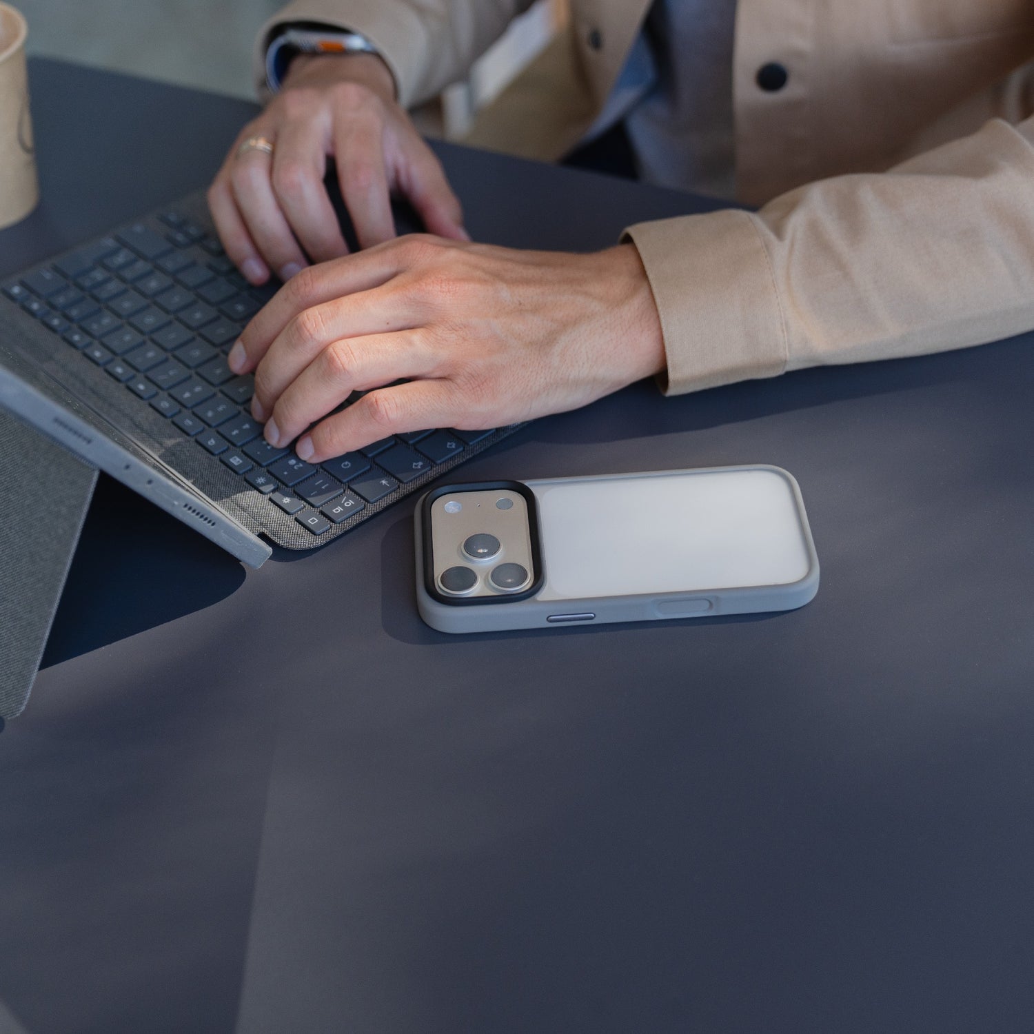 Eine Person, die an einem Schreibtisch auf einem Laptop tippt, mit einem Arktis iPhone 17 Pro Solid Case, das für sein mattes und stoßabsorbierendes Design bekannt ist, neben ihren Händen.