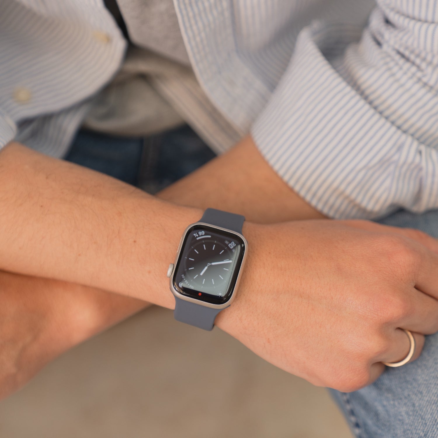 Eine Person trägt ein arktisband Apple Watch Silikonarmband "Sport" von arktisband in grau mit schweißabsorbierendem, sportlichem Design und analogem Zifferblatt am linken Handgelenk.