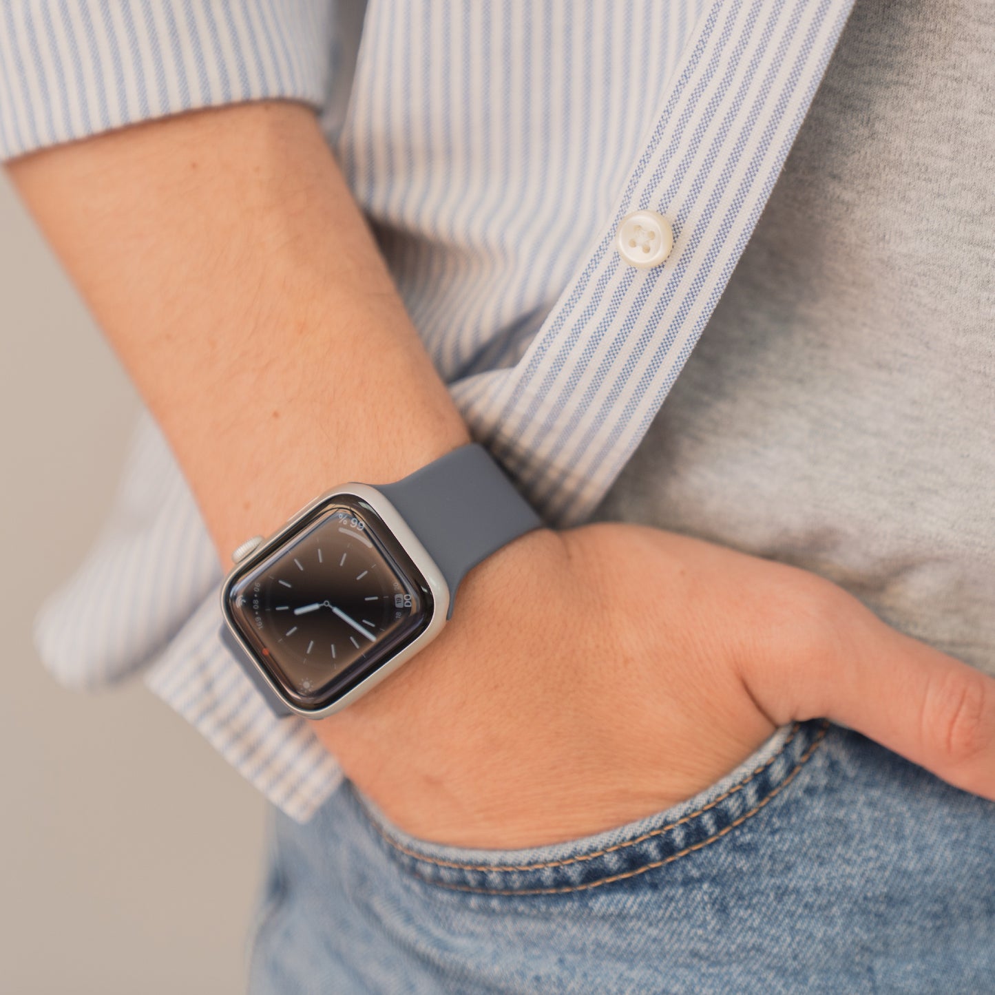 Eine Person trägt eine arktisband Apple Watch Silikonarmband "Sport" von arktisband mit blauem Band, Hand in der Tasche, bekleidet mit einer lässigen Jeans und einem gestreiften Hemd.