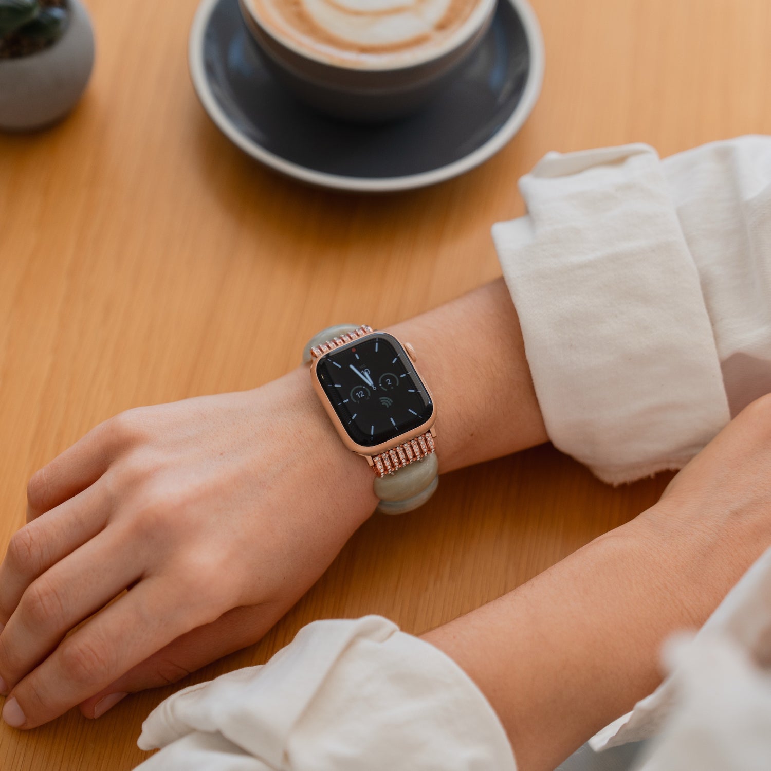 Jemand, der eine Apple Watch "Stone Pearl" von arktisband trägt, sitzt an einem Tisch mit einer Tasse Cappuccino.