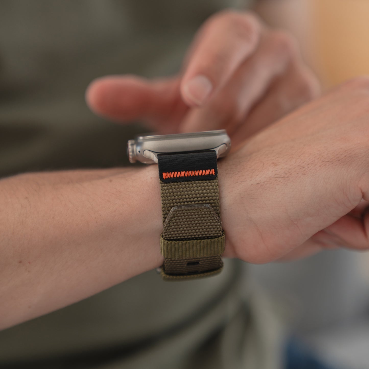 Eine Person trägt das arktisband Apple Watch Armband "Terra" (olivgrün, extrabreites 24 mm Nylonband) von arktisband auf ihrer Apple Watch Ultra und berührt dabei den Bildschirm der Uhr.