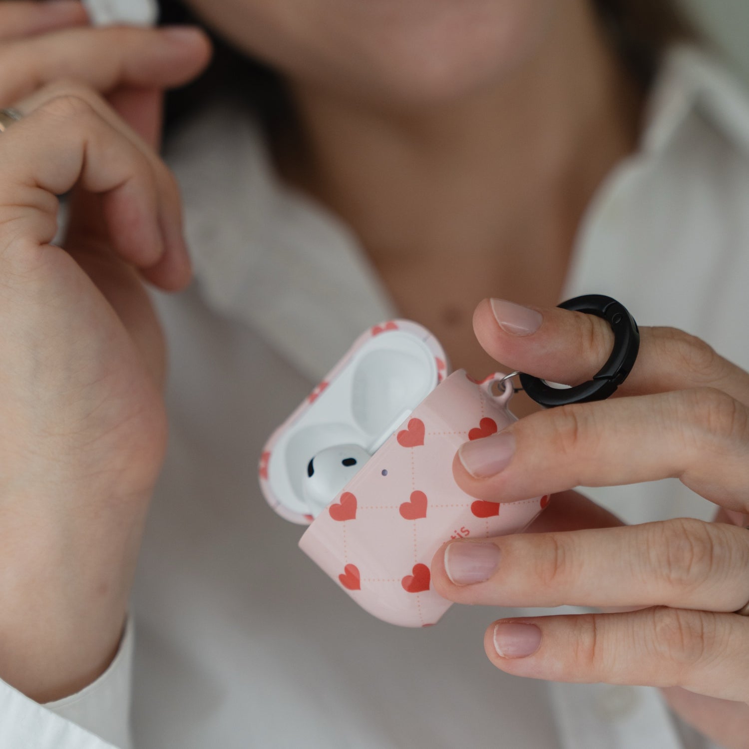 Eine Person hält eine Arktis AirPods 5 Hülle – Love Case mit Herzmuster und einem schwarzen Karabiner in der Hand.