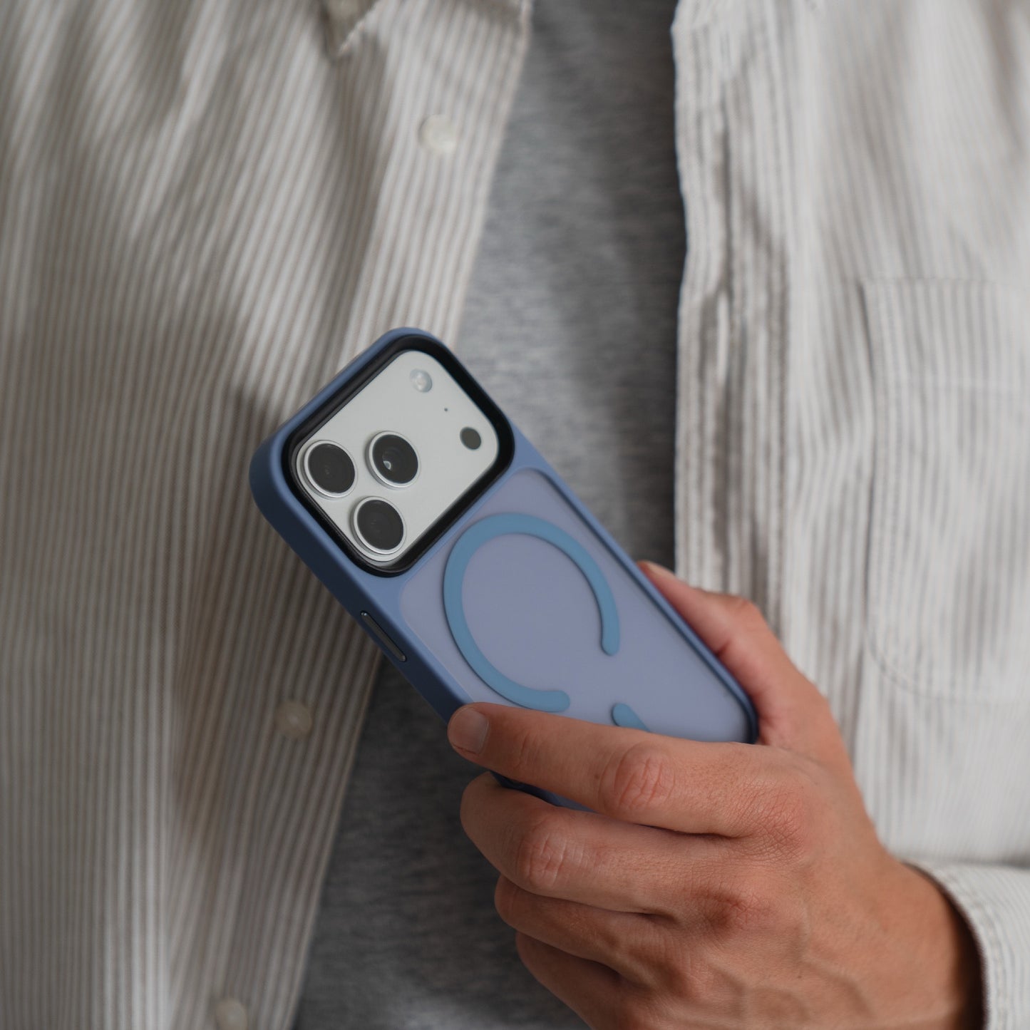 Eine Person mit weißem Hemd hält ein Arktis iPhone 17 Pro Solid Case mit MagSafe - eine blaue, matte Schutzhülle - und präsentiert dieses Arktis-Zubehör als ideale Wahl für Ihr iPhone 17 Pro.