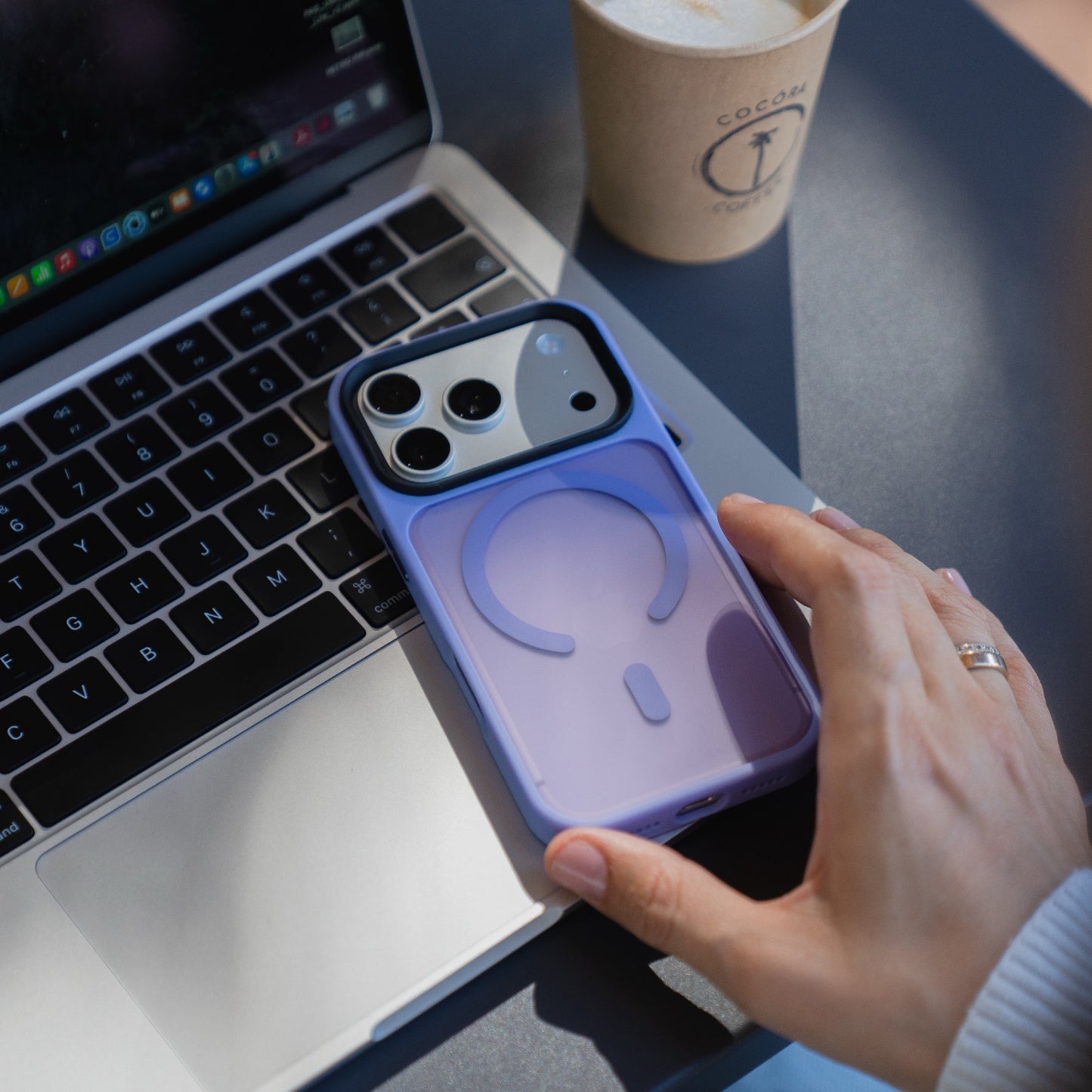 Eine Hand ruht auf einem Laptop neben einer Kaffeetasse; auf der Tastatur liegt ein Arktis iPhone 17 Pro Solid Case mit MagSafe, ein mattes lila Gehäuse von Arktis.