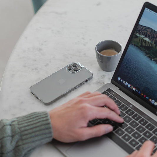 Eine Person im grünen Pullover tippt an einem runden Marmortisch auf einem Laptop. Daneben liegen ein graues Smartphone mit dem arktis Invisible Air Case von arktis und eine kleine Tasse Espresso.