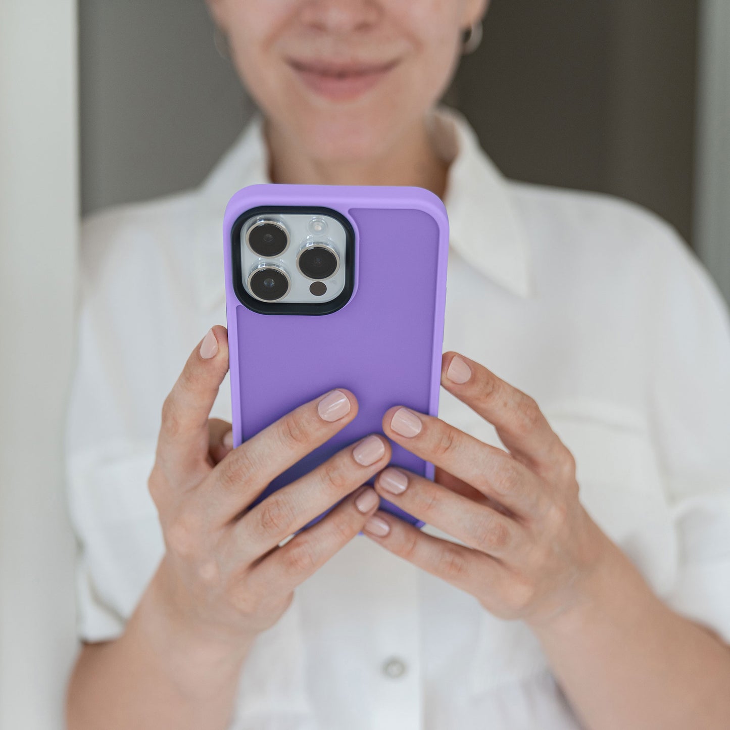 Frau im weißen Hemd lächelt sanft, während sie das MR PROTECT iPhone 13 Pro Case Matt, eine matte lila Schutzhülle von MR PROTECT, hält.