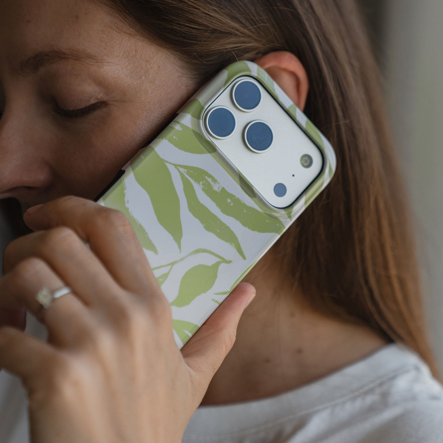 Eine Frau im weißen Hemd hält ein iPhone 14 Pro Max mit der arktis iPhone 14 Pro Max Hülle - Botanic, einer grünen, blattgemusterten, stoßabsorbierenden TPU-Silikonhülle, an ihr Ohr.