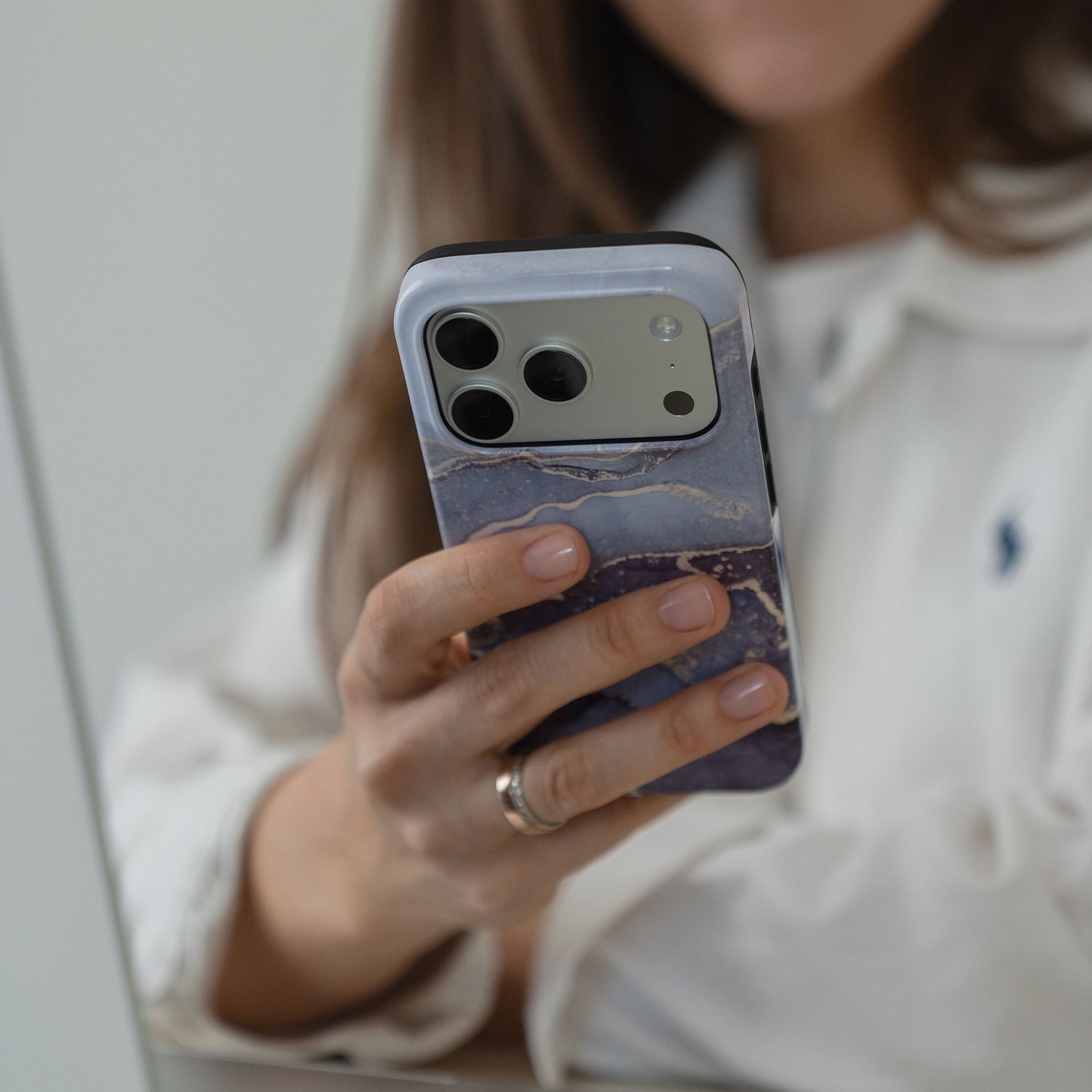 Eine Person hält ein arktis iPhone 14 Pro Max Hülle - Dusty Marble aus stoßabsorbierendem TPU-Silikon, während sie ein weißes Hemd mit Polo-Logo trägt.