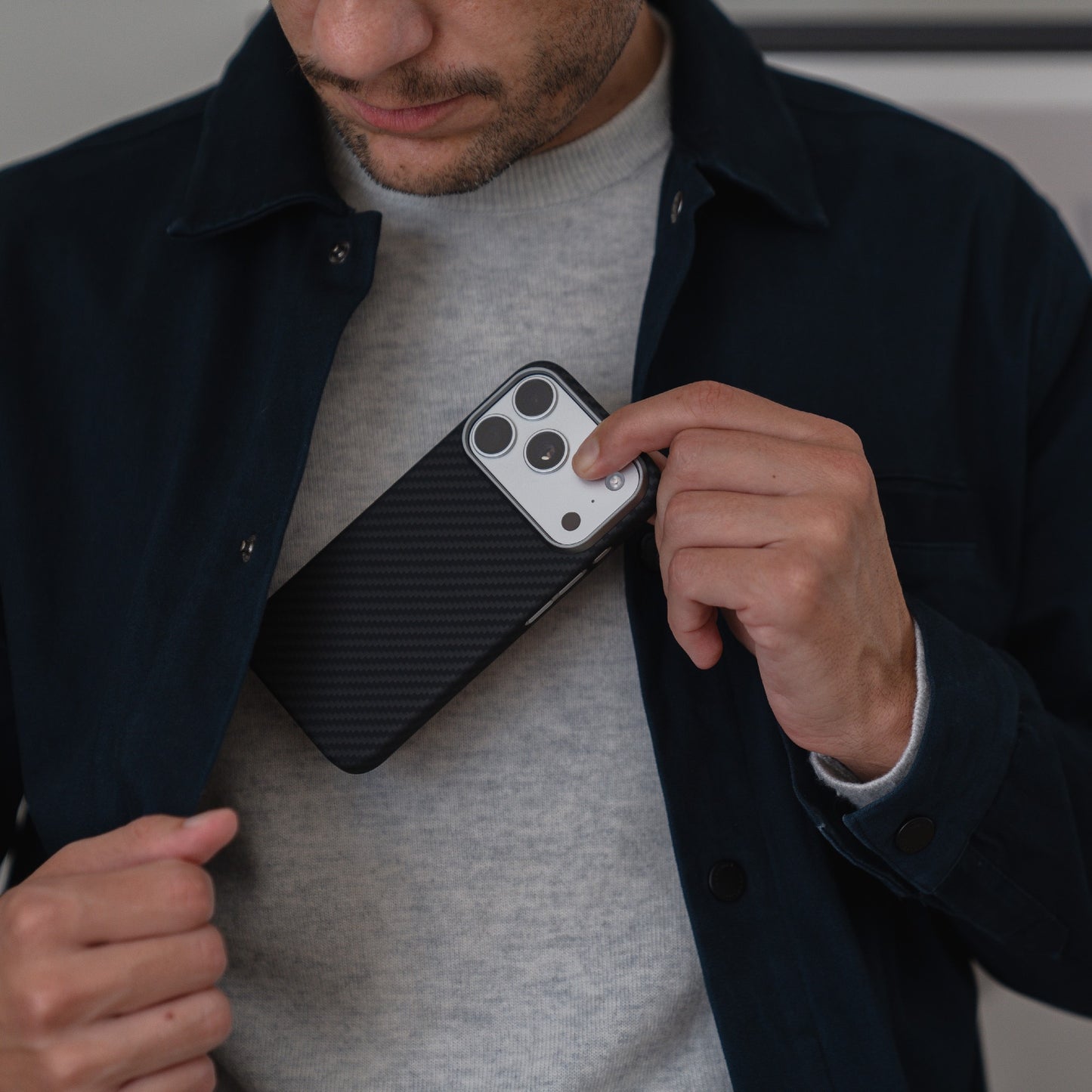 Ein Mann steckt sein mit einem arktis iPhone 17 Pro Carbon Case geschütztes Smartphone in die Innentasche seiner dunklen Jacke.
