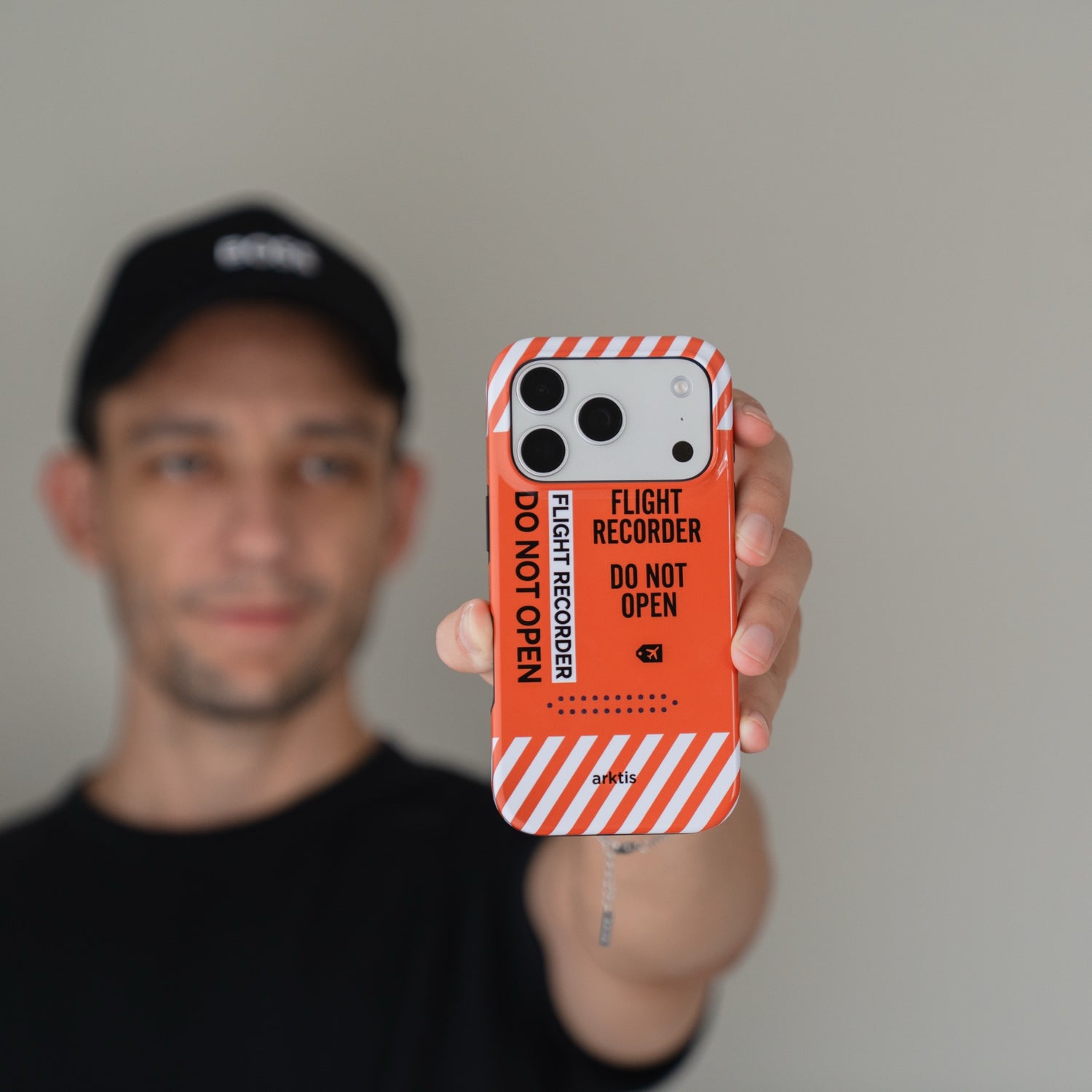 Eine Person, die eine Arktis iPhone 18 Pro Airport-Hülle mit der Aufschrift FLIGHT RECORDER DO NOT OPEN in der Hand hält, die zur Kamera zeigt.