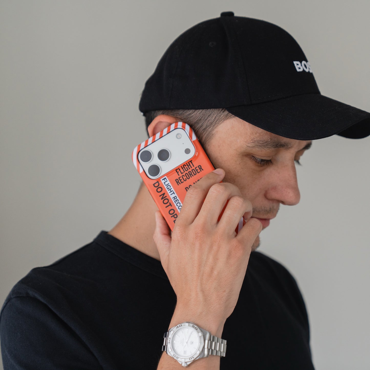 Ein Mann in schwarzem Hemd und mit einer Mütze, der eine Arktis iPhone 16e Airport-Hülle mit der Aufschrift FLIGHT RECORDER DO NOT OPEN in der Hand hält.