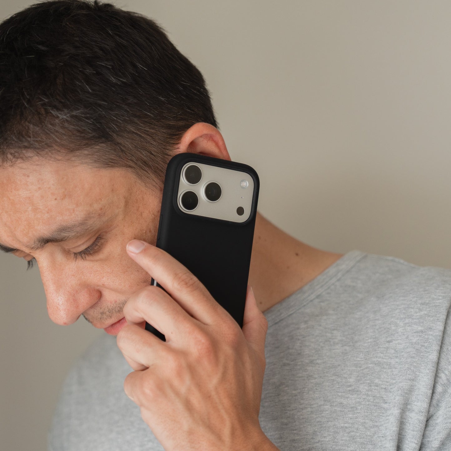 Ein Mann in einem grauen Hemd hält eine Arktis iPhone 18 Pro Silikonhülle mit MagSafe, schwarz ans Ohr und telefoniert.