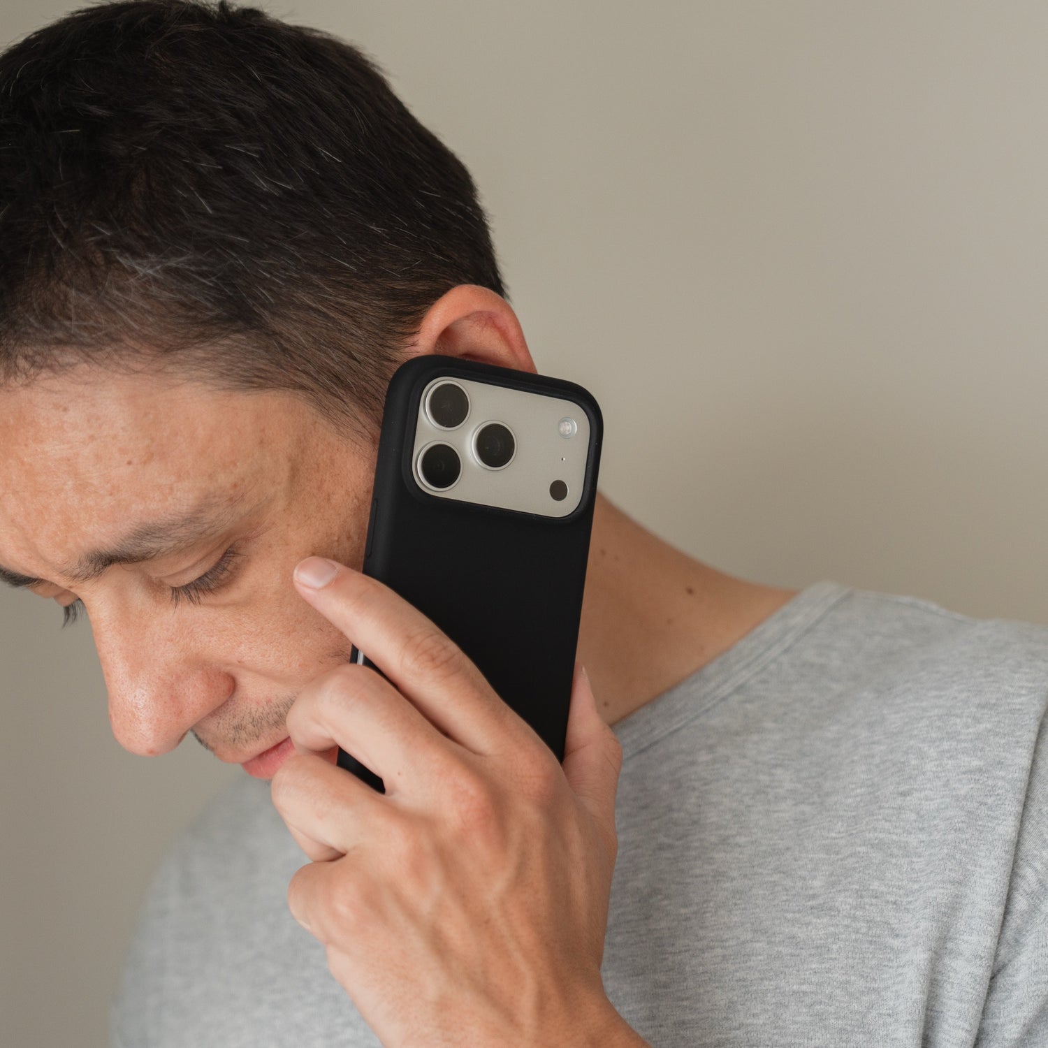 Ein Mann in einem grauen Hemd hält eine Arktis iPhone 18 Pro Silikonhülle mit MagSafe, schwarz ans Ohr und telefoniert.