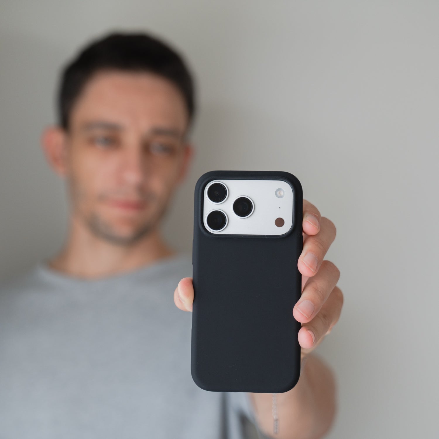 Eine Person hält eine Arktis iPhone 18 Pro Silikonhülle mit MagSafe, schwarz in der Hand, während das Gesicht im Hintergrund unscharf dargestellt ist.