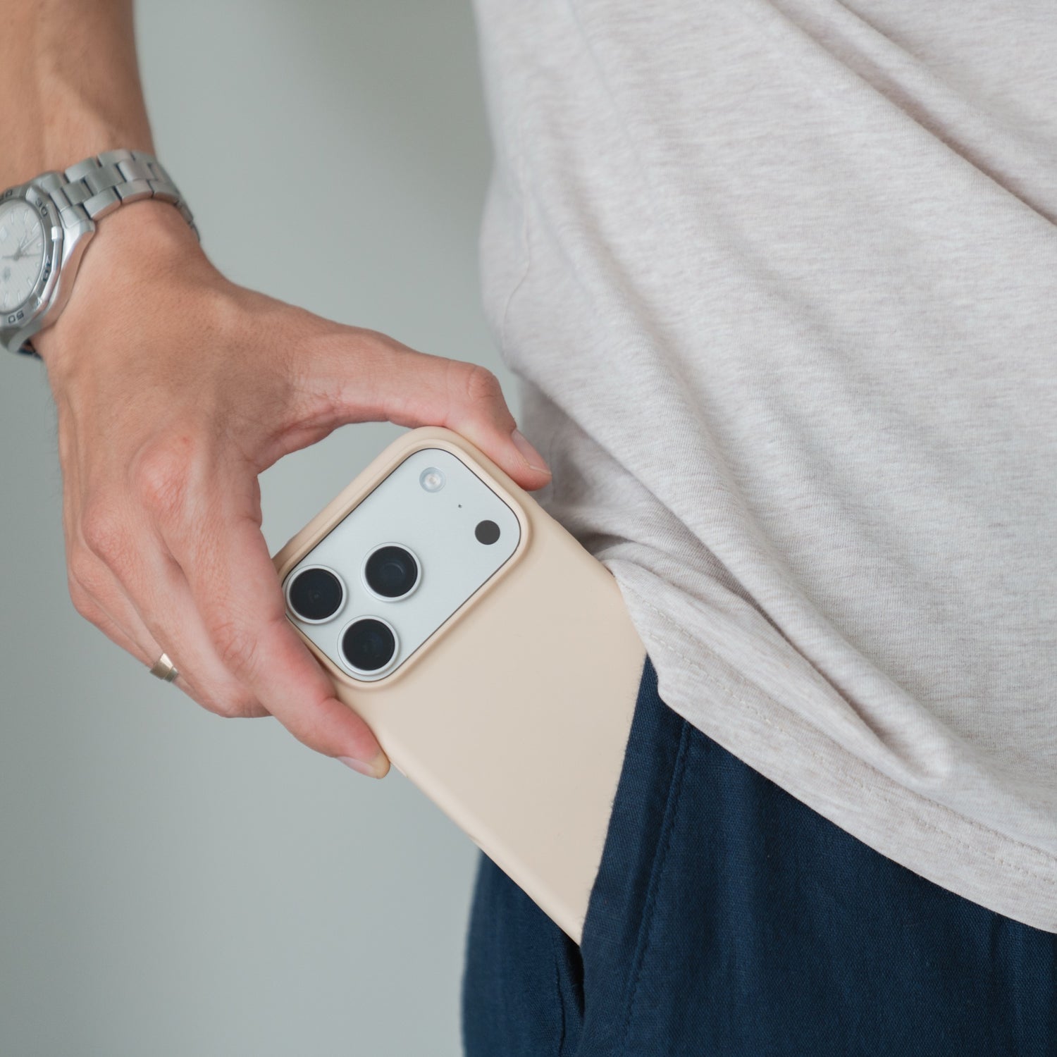 Die Hand mit der Arktis-Silikonhülle für das iPhone 18 Pro Max mit MagSafe lässt das Handy in die dunkle Hosentasche gleiten. Helles Hemd, Uhr sichtbar.