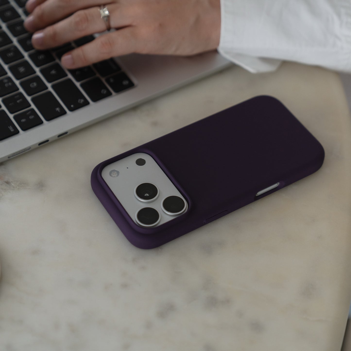 Eine Arktis iPhone 18 Pro Max-Silikonhülle mit MagSafe in Nebelviolett liegt auf einem Marmortisch neben einer Person, die gerade einen Laptop benutzt.