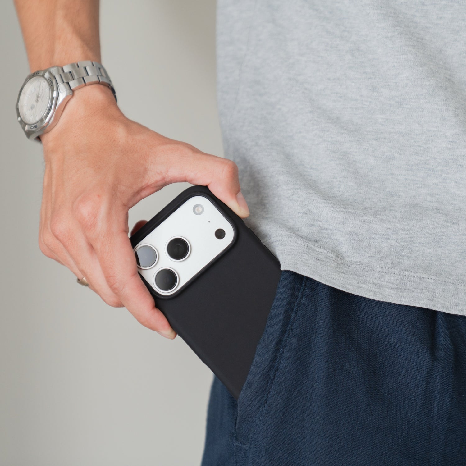 Jemand, der eine Armbanduhr trägt, steckt eine Arktis iPhone 18 Pro Silikonhülle mit MagSafe, Schwarz in die Tasche seiner marineblauen Hose.