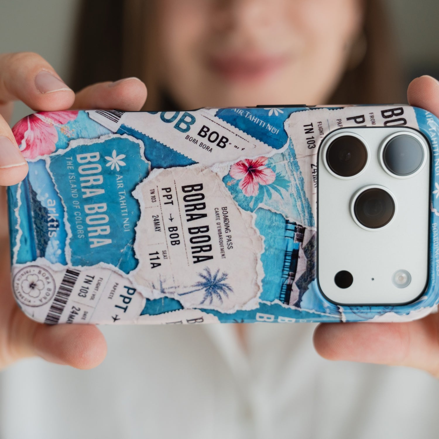 Jemand hält eine Arktis iPhone 16e – Happy Island-Hülle mit Motiven zum Thema Bora Bora und Bordkarten in der Hand.