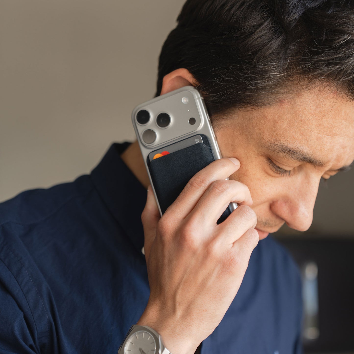 Mann im marineblauen Hemd hält sein Smartphone mit einem arktis iPhone MagSafe Kartenhalter aus Alcantara an sein Ohr.