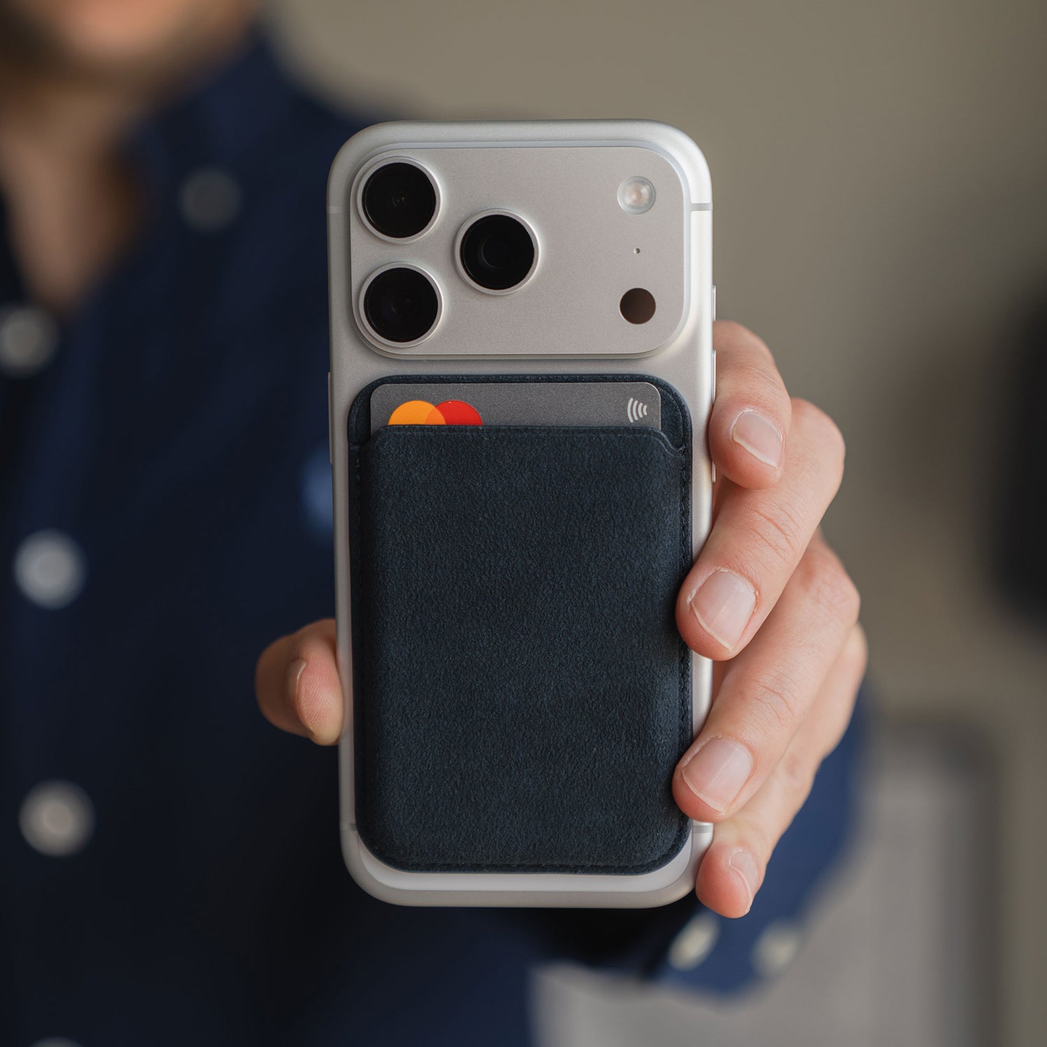 Eine Person hält ein iPhone, an dem der arktis iPhone MagSafe Kartenhalter aus Alcantara von arktis befestigt ist, und zeigt eine teilweise sichtbare Kreditkarte.