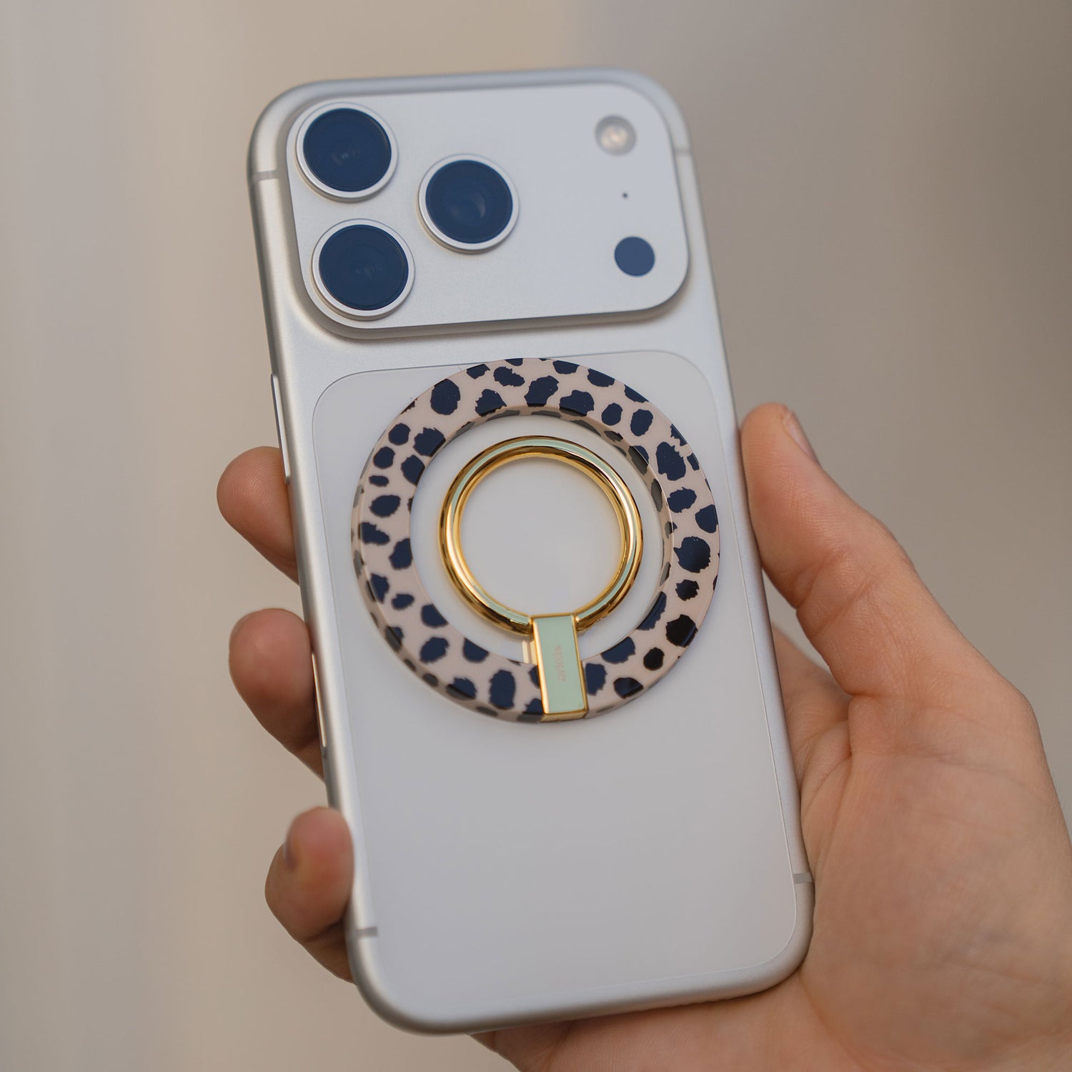 Eine Hand hält einen arktis Magnetischer Ringhalter für MagSafe - Sweet Leopard mit robuster N52 Magnete auf einem silbernen iPhone - stylisches, praktisches Zubehör für Ihr Gerät.