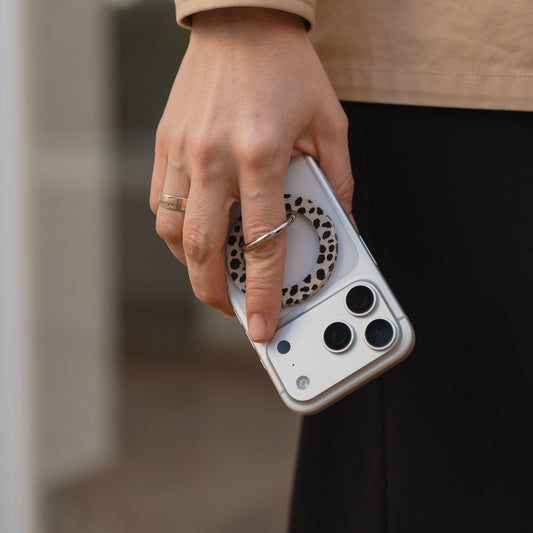 Eine Hand hält ein weißes Smartphone mit dreifacher Kamera auf der Rückseite und einem arktis Magnetischer Ringhalter für MagSafe - Sweet Leopard, mit starken N52 Magneten.