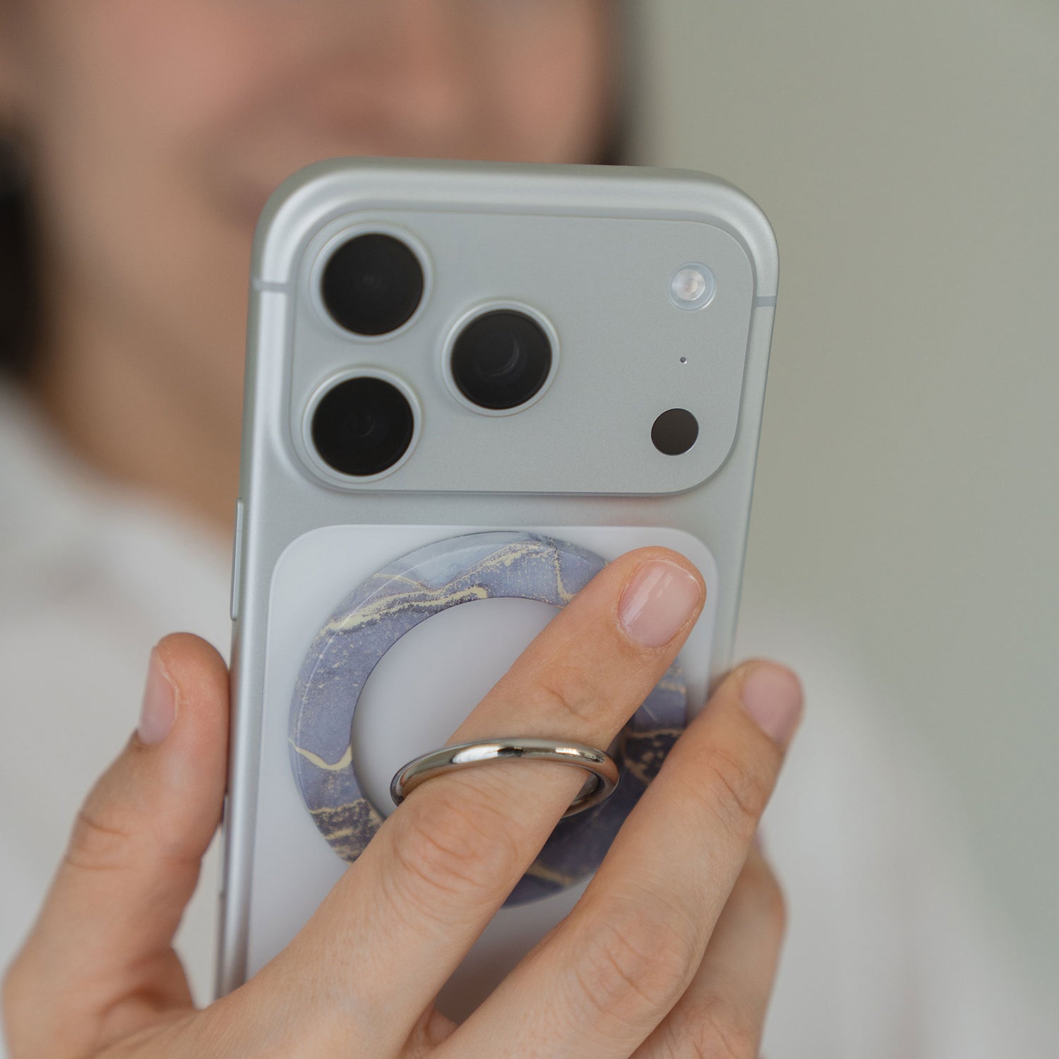 Eine Hand hält ein Smartphone, an dem der arktis Magnetischer Ringhalter für MagSafe - Sweet Leopard mit starken N52 Magneten befestigt ist; das iPhone Zubehör ist mit den Kameralinsen im Fokus hervorgehoben.