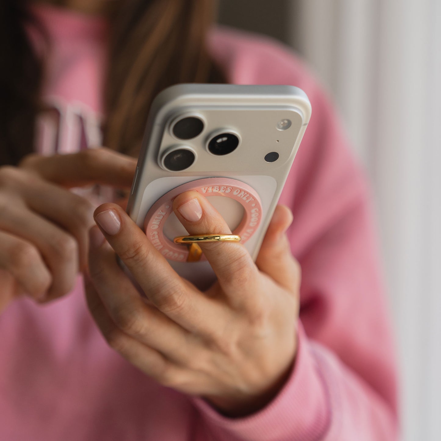 Eine Person in einem rosa Pullover hält ein Smartphone mit dem arktis Magnetischer Ringhalter für MagSafe - Good Vibes auf der Rückseite.