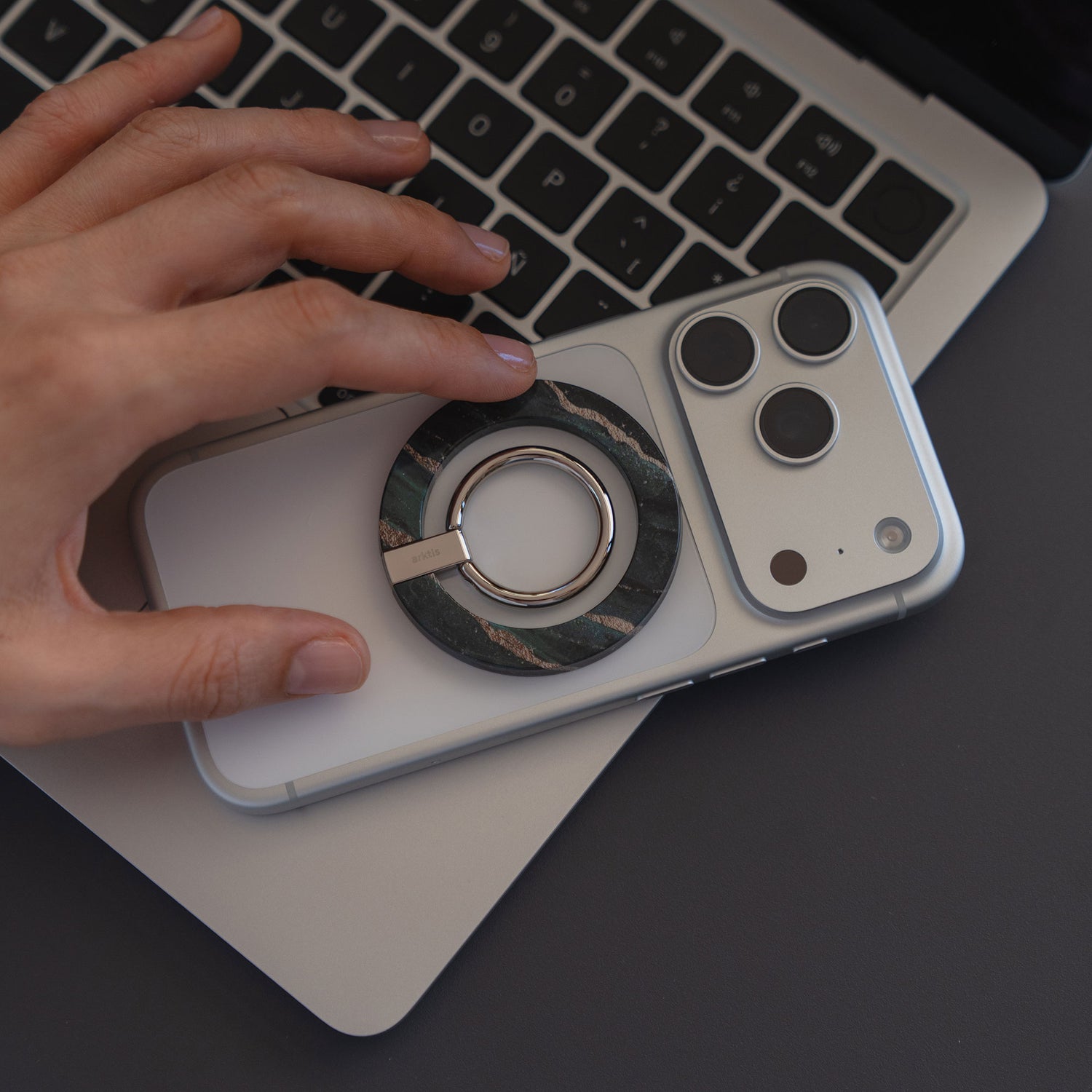 Eine Hand berührt ein iPhone mit dem arktis Magnetischer Ringhalter für MagSafe - Sweet Leopard, das auf einem Laptop-Tastatur-stylischen Zubehör mit starken N52 Magneten für einen sicheren Halt ruht.