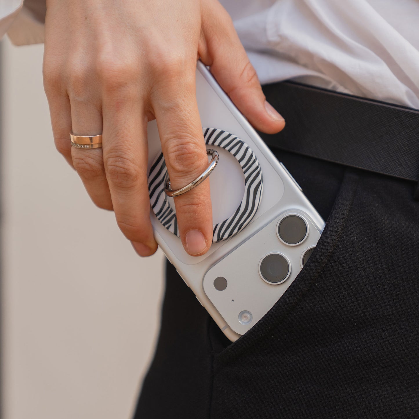Handeinlegen eines weißen Smartphones mit dem arktis Magnetischer Ringhalter für MagSafe - Sweet Leopard in eine schwarze Hosentasche - stylisches iPhone Zubehör mit starken N52 Magneten für sicheren Halt.