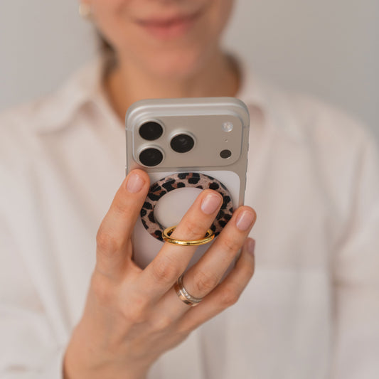 Jemand hält einen arktis iPhone MagSafe Ring Halter mit Leopardenprint und stylt sein Outfit mit einem weißen Hemd und einem goldenen Ring. Starke N52-Magnete von arktis halten den Griff sicher und modisch zugleich.
