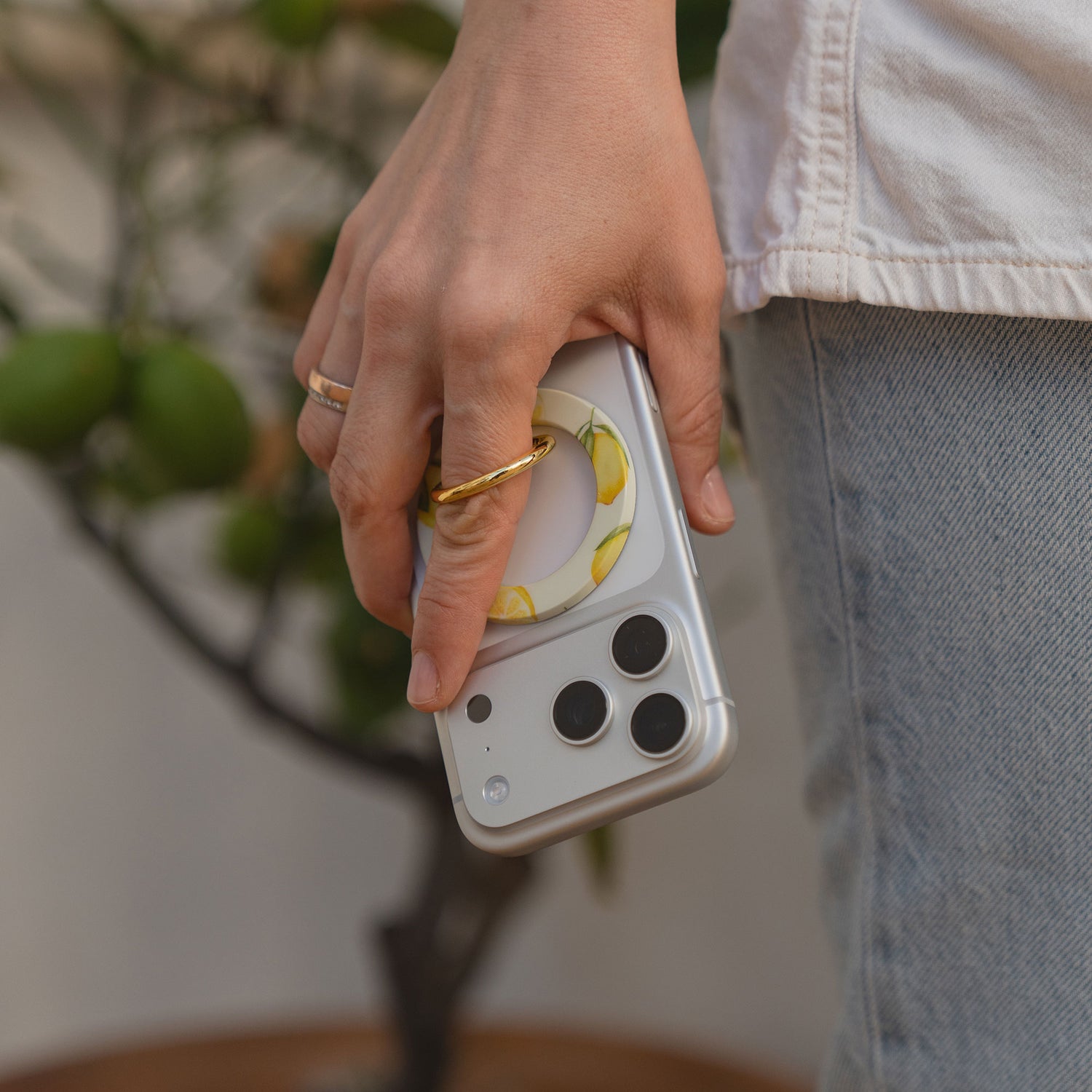 Eine Hand hält ein silbernes Smartphone mit dem arktis Magnetischer Ringhalter für MagSafe - Sweet Leopard, mit N52 Magnete, neben jemandem in Jeans-stylischem und sicherem iPhone Zubehör für erhöhten Halt.
