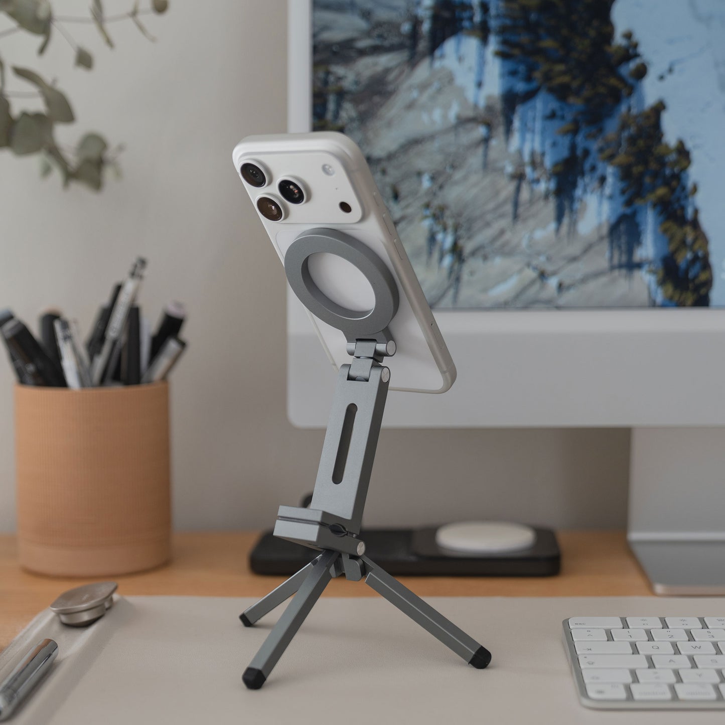 Ein iPhone auf der arktis iPhone MagSafe Tripod 360 Halterung liegt auf einem Schreibtisch vor einem Computermonitor und einer Tastatur.