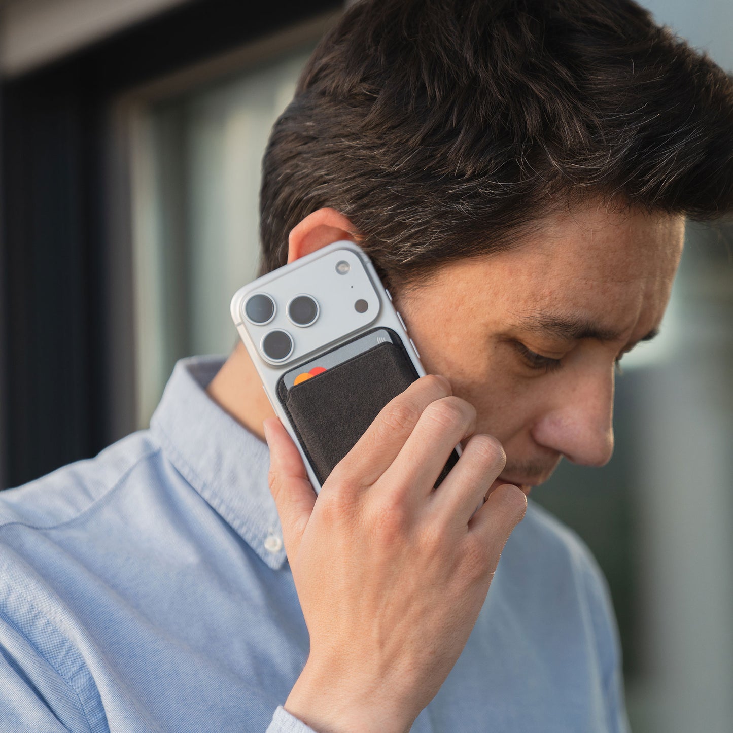 Ein Mann hält sein iPhone mit dem auf der Rückseite angebrachten arktis iPhone MagSafe Kartenhalter aus Alcantara an sein Ohr, als würde er telefonieren.