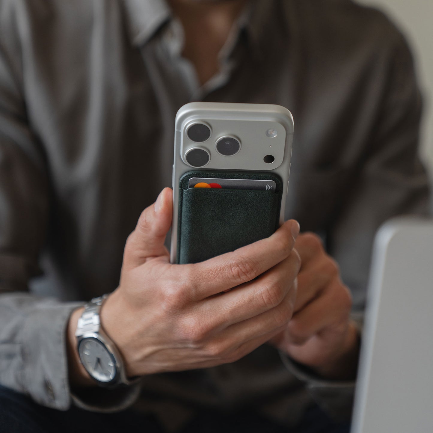 Eine Person hält ein iPhone 12 mit dem arktis iPhone MagSafe Kartenhalter aus Alcantara von arktis in der Hand, eine Kreditkarte ist teilweise sichtbar.