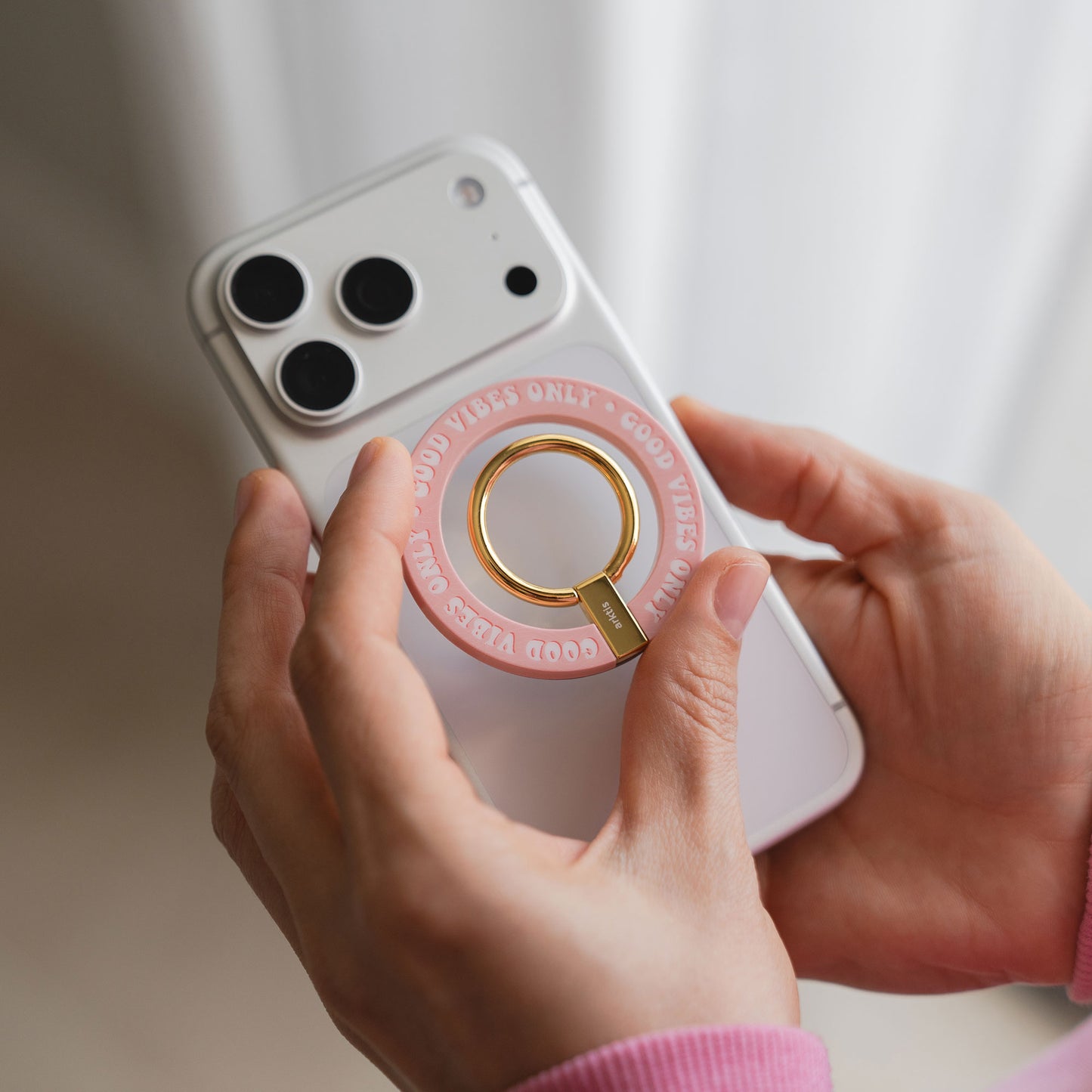 Die Hände halten ein weißes Telefon mit dem arktis Magnetischer Ringhalter für MagSafe - Good Vibes, mit goldenem "GOOD VIBES ONLY"-Text - ein stilvolles, positives iPhone-Zubehör für den täglichen Gebrauch.