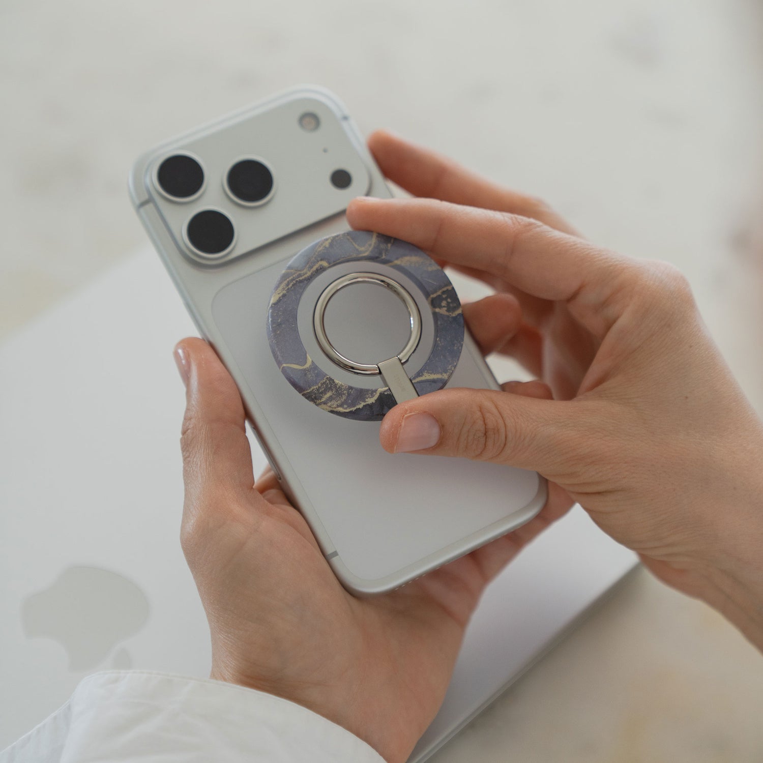 In den Händen hält man ein weißes Smartphone mit dem auf der Rückseite angebrachten arktis Magnetischer Ringhalter für MagSafe - Sweet Leopard, der als stylisches iPhone Zubehör elegantes Leoparden-Design und praktische Funktionalität vereint.