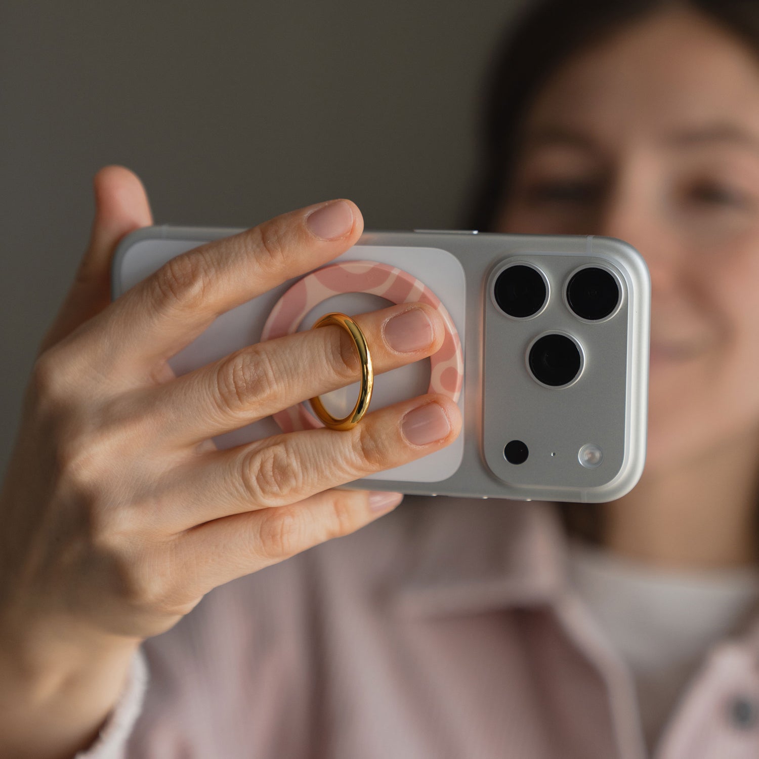 Person, die ein Smartphone mit dem goldenen arktis Magnetischer Ringhalter für MagSafe - Curly hält, nimmt ein Selfie auf, das Gesicht ist unscharf - ein stilvolles iPhone Zubehör mit starken N52-Magneten für einen sicheren Halt.