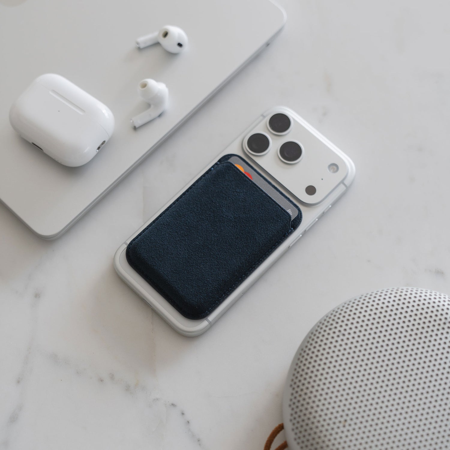 Arktis iPhone MagSafe Kartenhalter aus Alcantara, kabellose Ohrhörer und Lautsprecher neben einem Smartphone auf weißer Oberfläche.