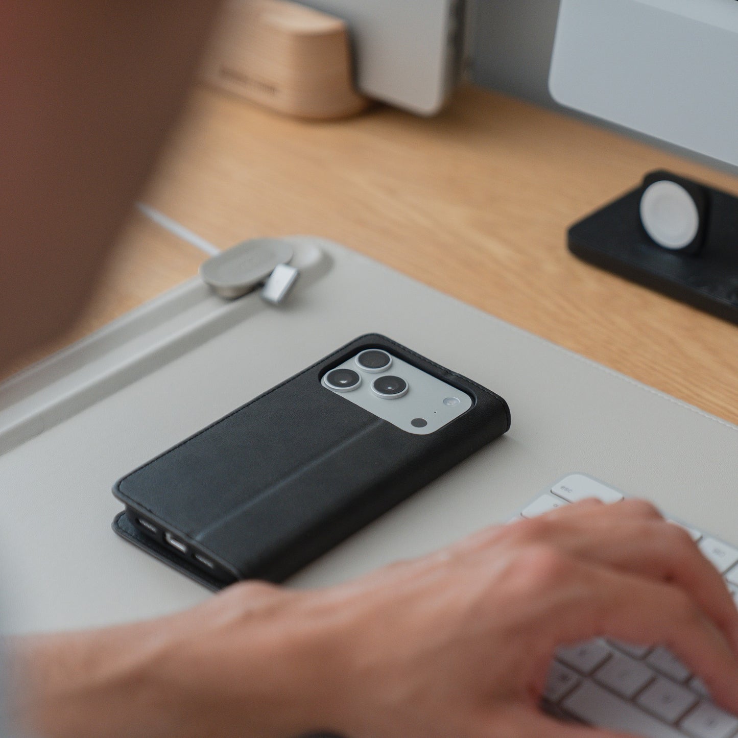 Person tippt auf einer Tastatur, daneben ein Smartphone in der eleganten arktis iPhone 17 Pro Book Case Kunstlederhülle auf dem Schreibtisch - die perfekte Hülle von arktis für das iPhone 17 Pro.